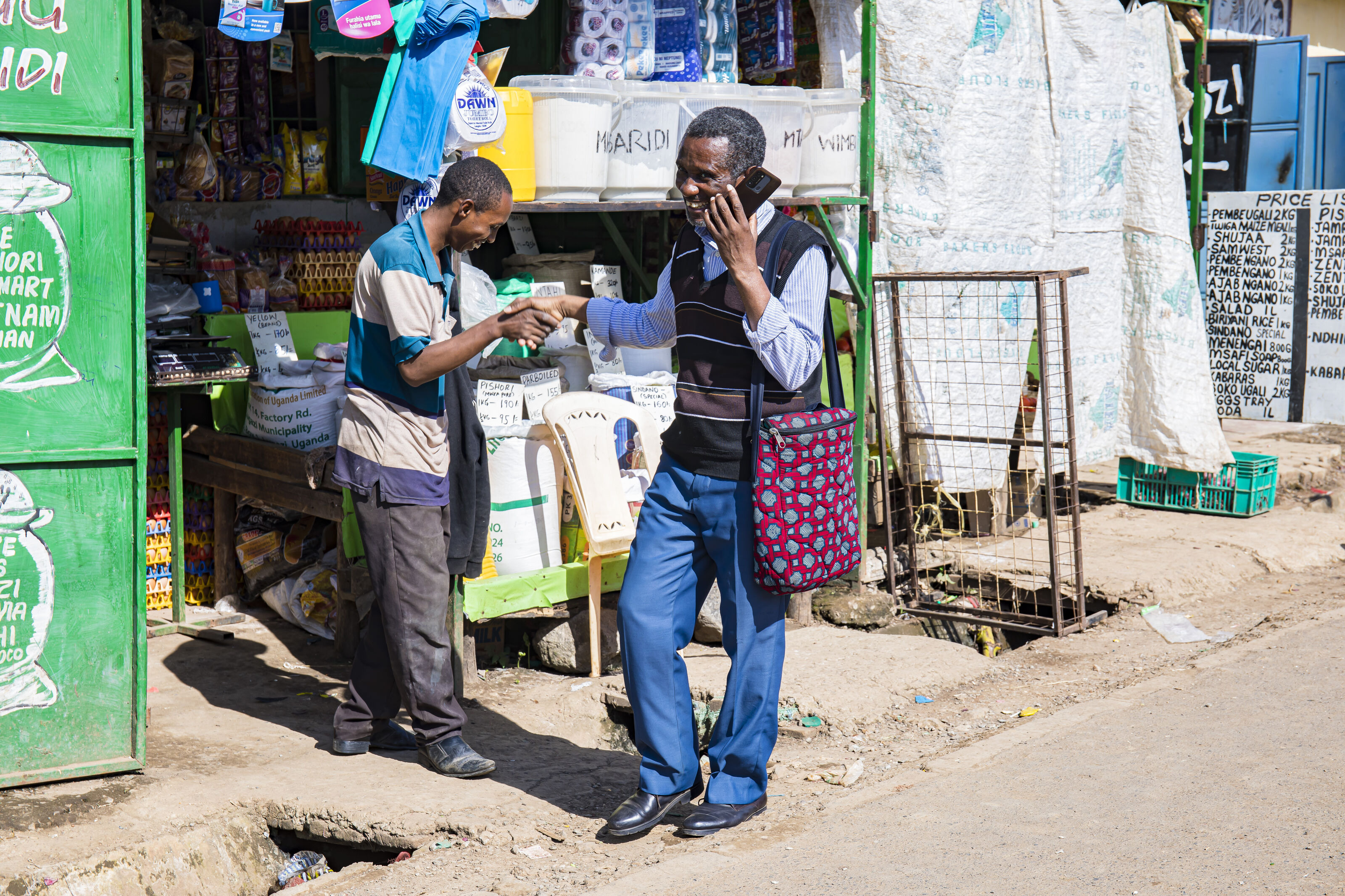 Celestin Mbaruku stands beside a sewing trainee and helps to align the fabric on the sewing machine. (Nairobi, Kenya 2024)