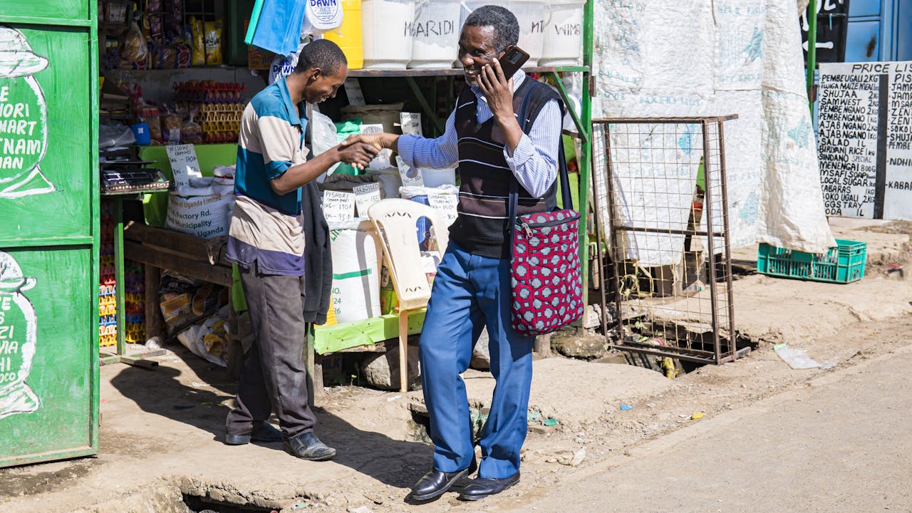 Celestin Mbaruku stands beside a sewing trainee and helps to align the fabric on the sewing machine. (Nairobi, Kenya 2024)