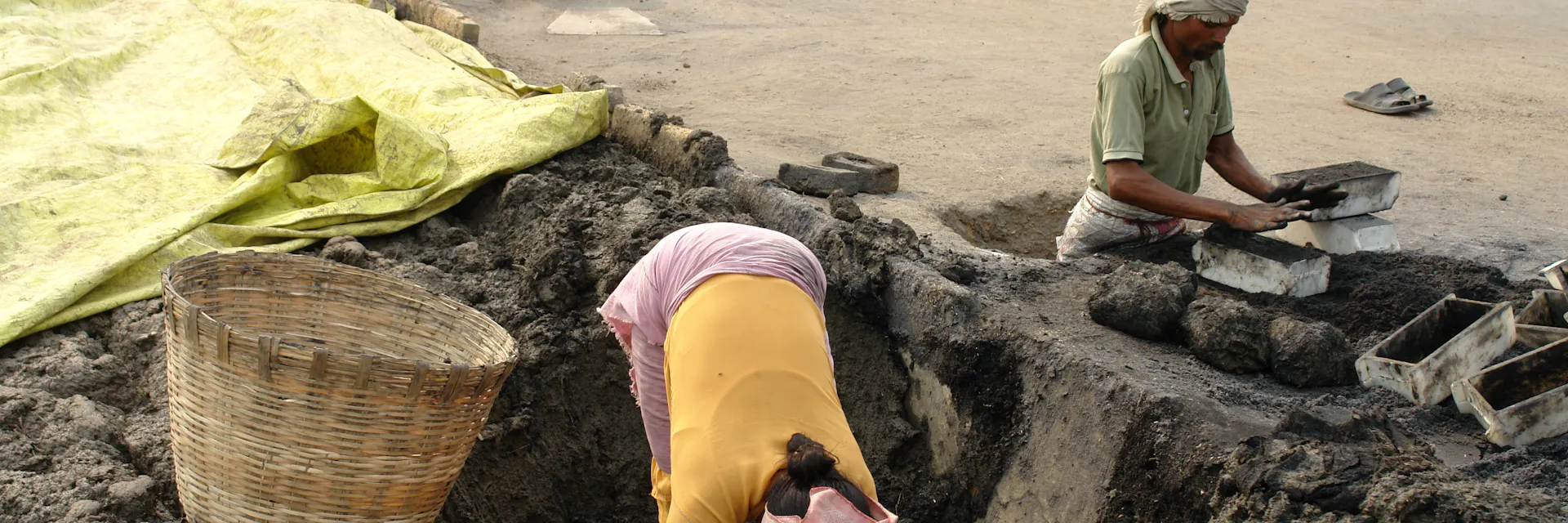 Deux ouvriers d'une briqueterie de l'Andhra Pradesh, en Inde, en situation de servitude pour dettes, creusent la terre pour la mettre dans des moules à briques. D'autres travailleurs et des piles de briques se trouvent à l'arrière-plan. (2013)