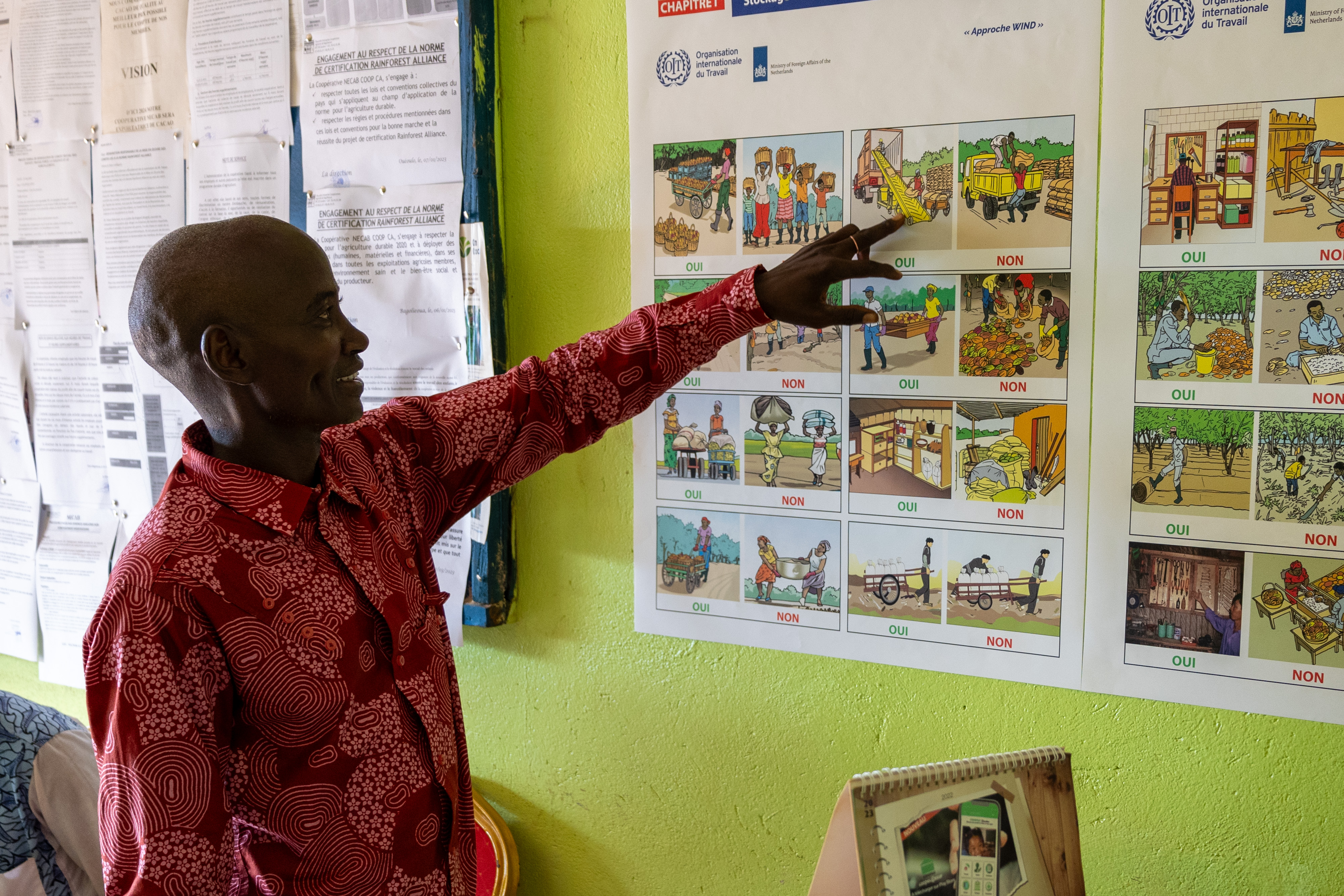 Yabao Oumarou points to posters displayed on the wall. The posters show how plantation workers can improve safety and health at work. (2024).