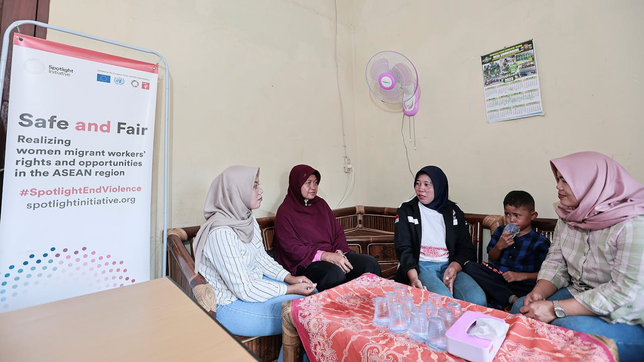 Win Faidah est assise avec son fils au Centre de ressources pour les travailleurs migrants. Elle discute avec trois autres femmes assises autour d’une table. 