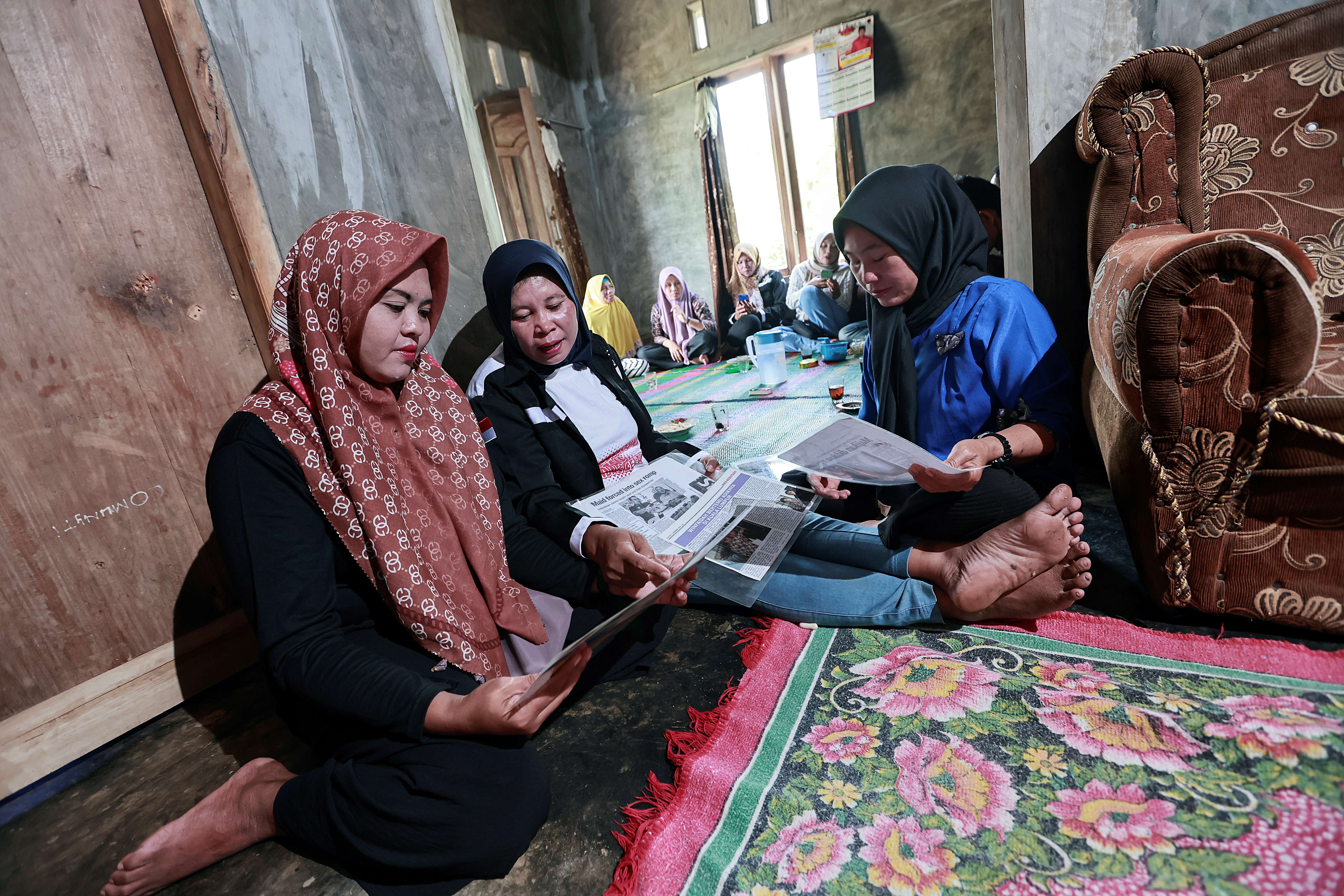 Win Faidah sits on the floor between two other women. Together they look at newspaper articles about her experience.