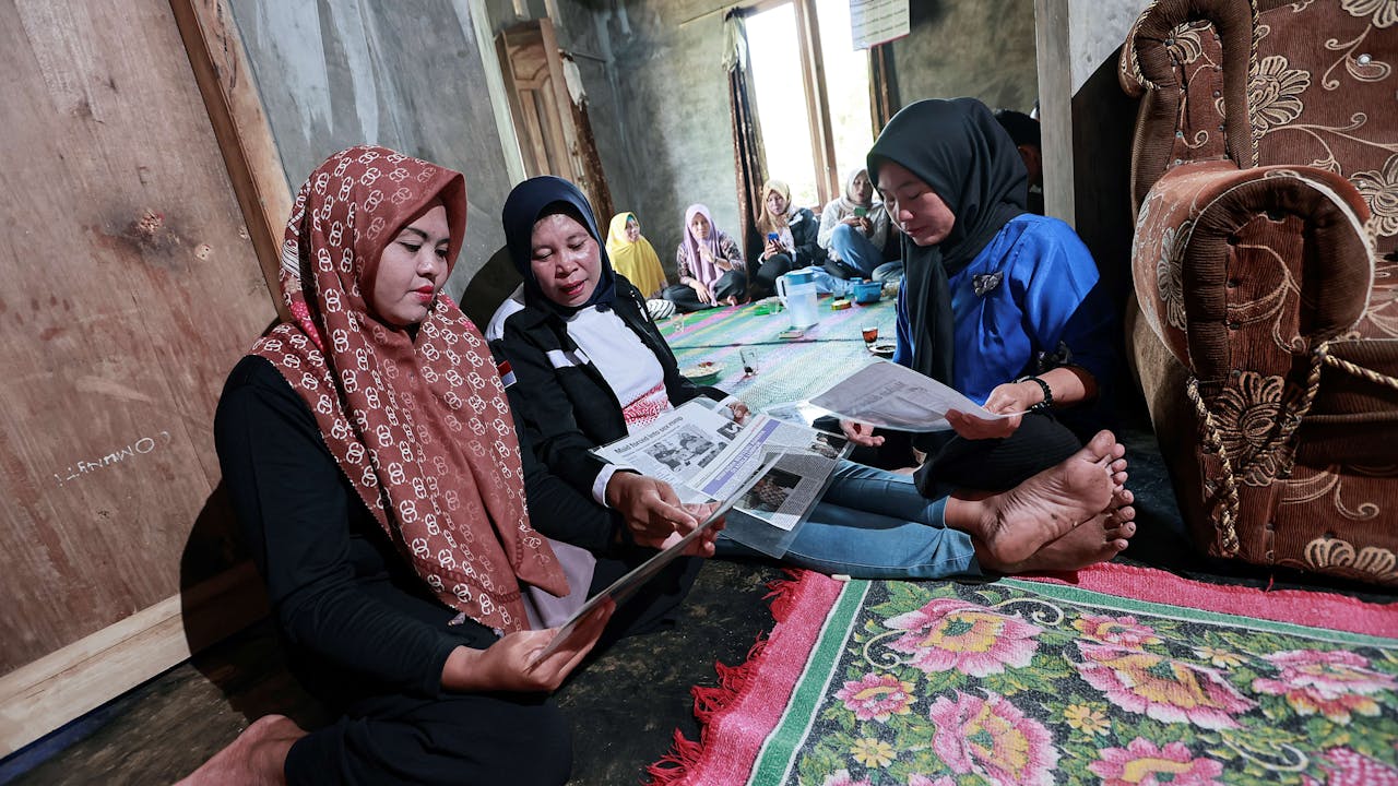 Win Faidah sits on the floor between two other women. Together they look at newspaper articles about her experience.