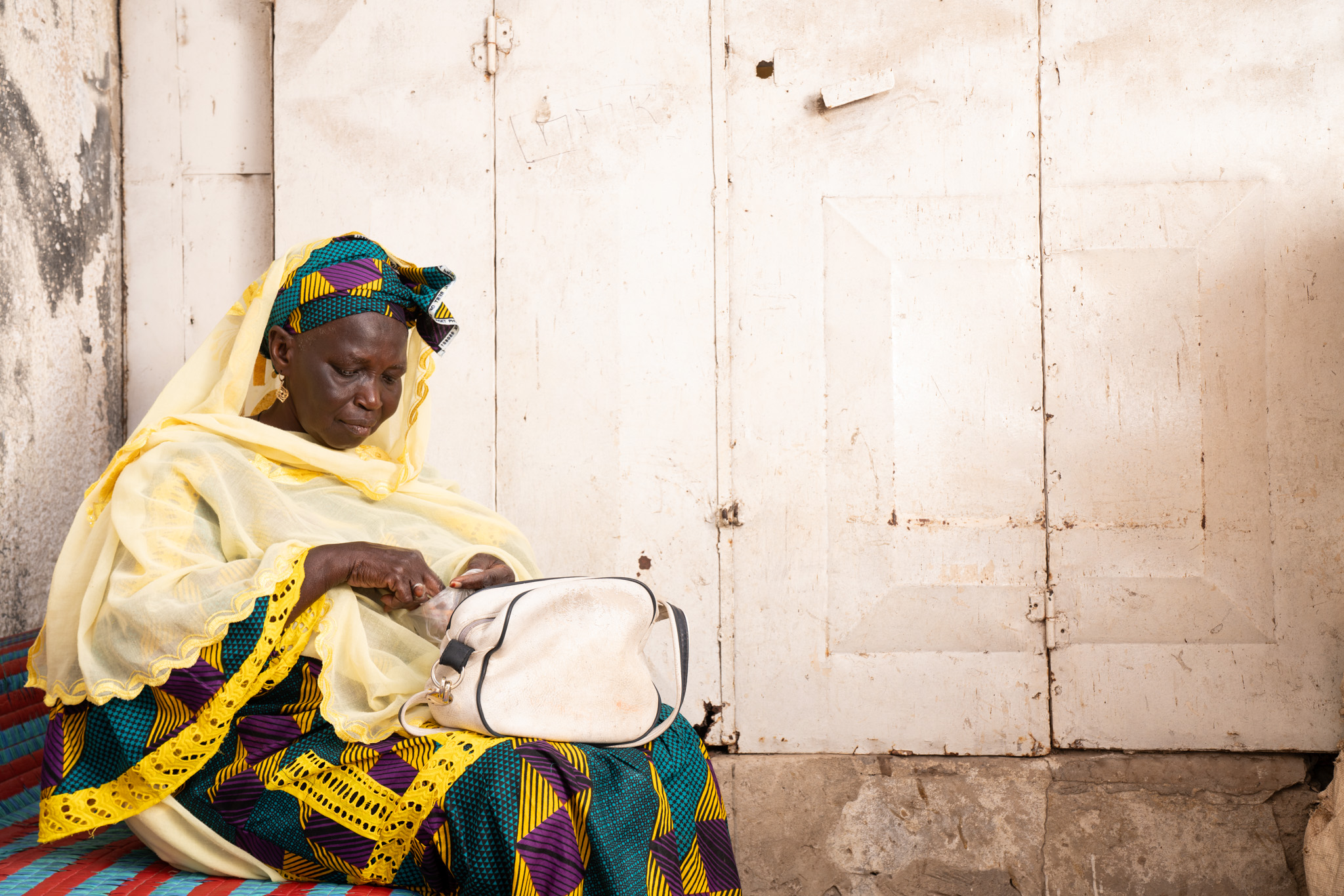 Astou Gningue sits on a seat and counts money from a small bag. Pikine, Senegal.(2024)