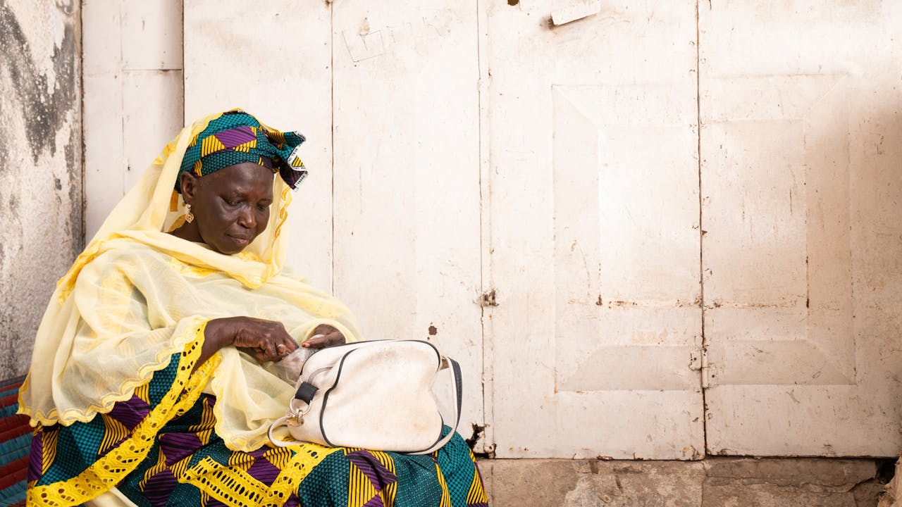 Astou Gningue sits on a seat and counts money from a small bag. Pikine, Senegal.(2024)
