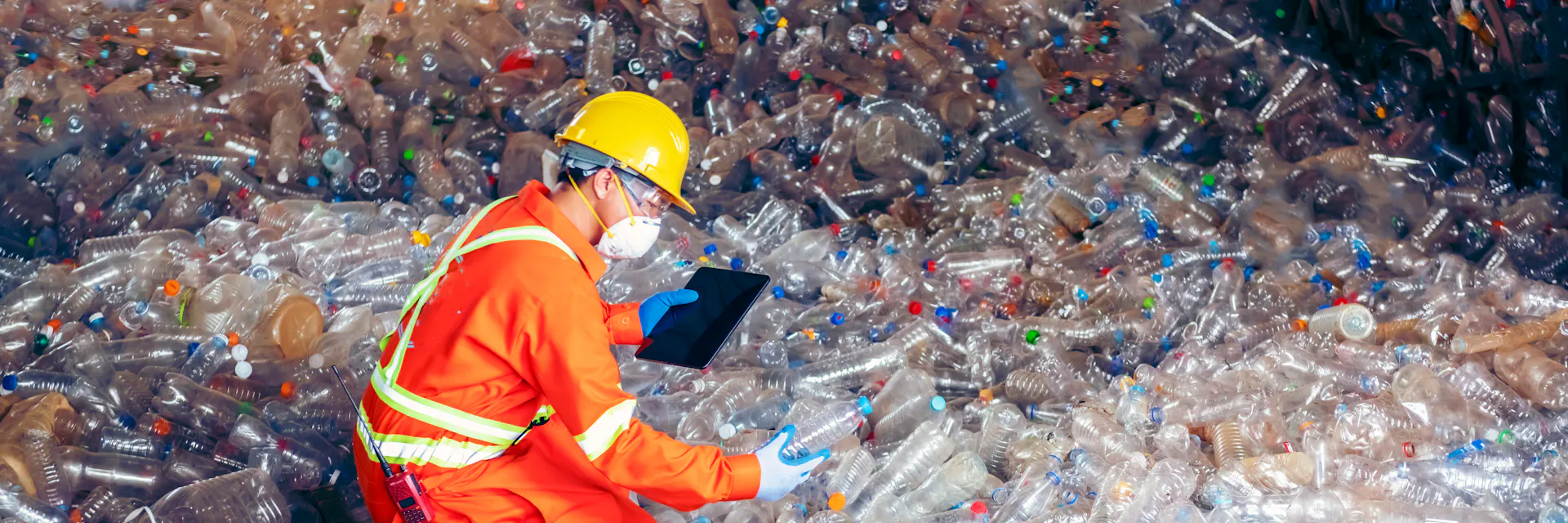 Man in orange uniform is examining plastic bottles in the recycling centre. Recycling industry.
