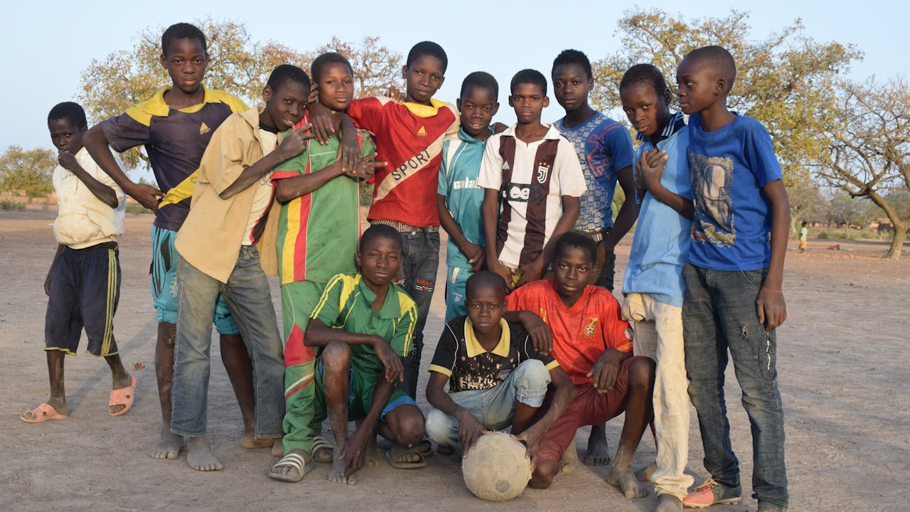 Domboué Nibéissé poses for the camera outside with a group of boys.  One of the boys holds a football.