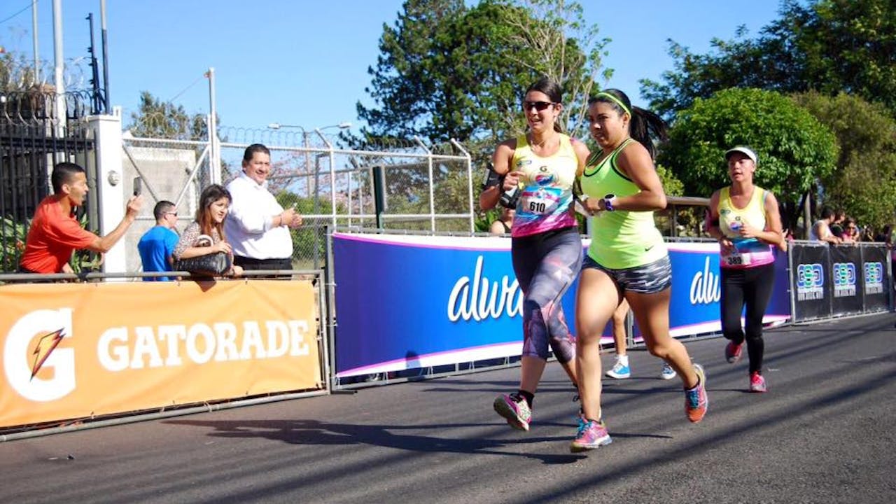 Güler Koca runs alongside a sighted runner at a marathon. She is smiling. People on the side-lines cheer them on.