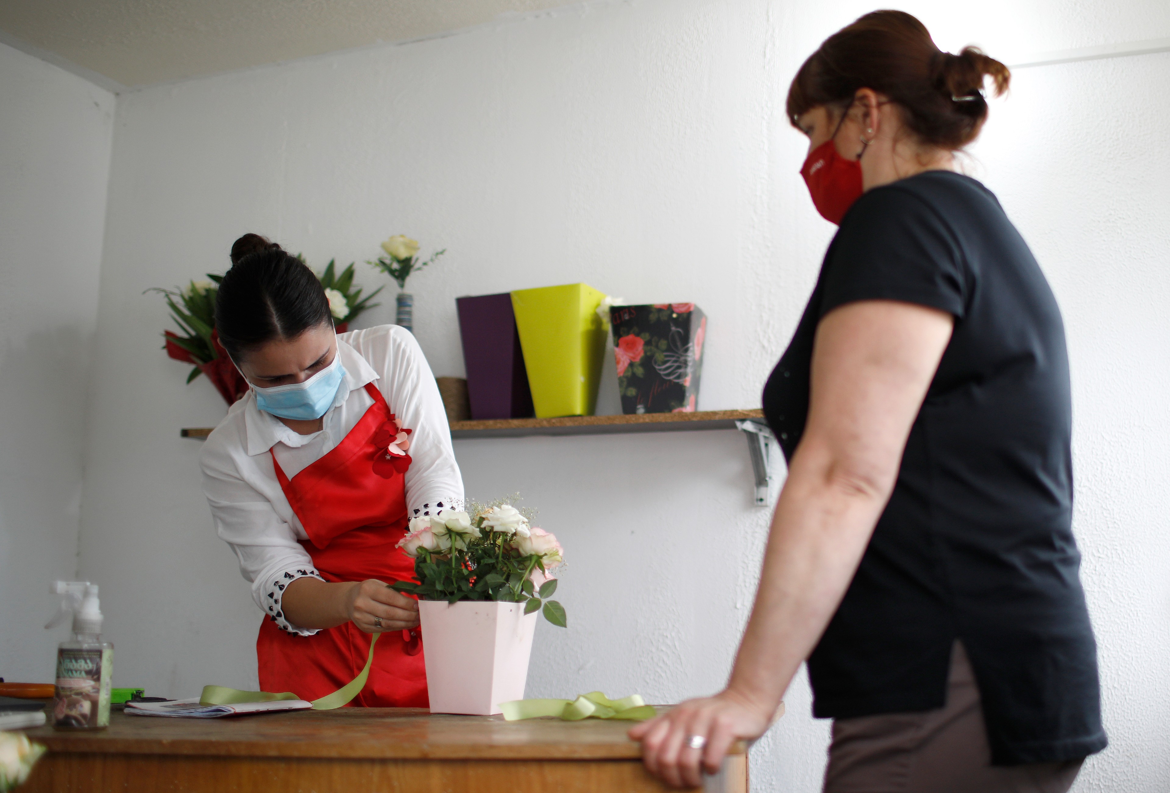 Mariam Kobalia prepares white roses in a vase for a customer.  Both Mariam and the customer wear a mask. 