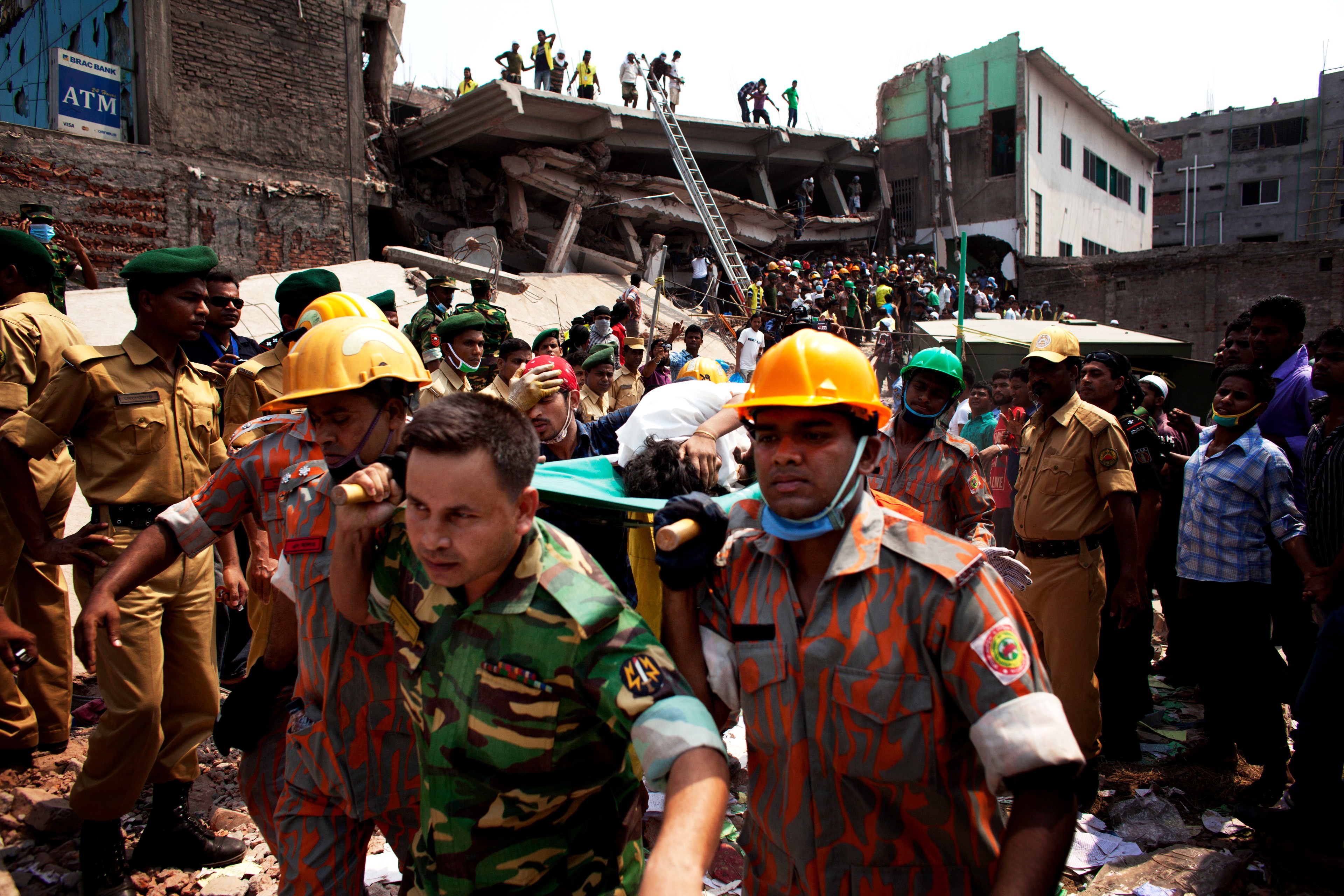 Members of Dhaka’s fire service carry an injured woman away from the rubble. In the background is the collapsed Rana Plaza building. 