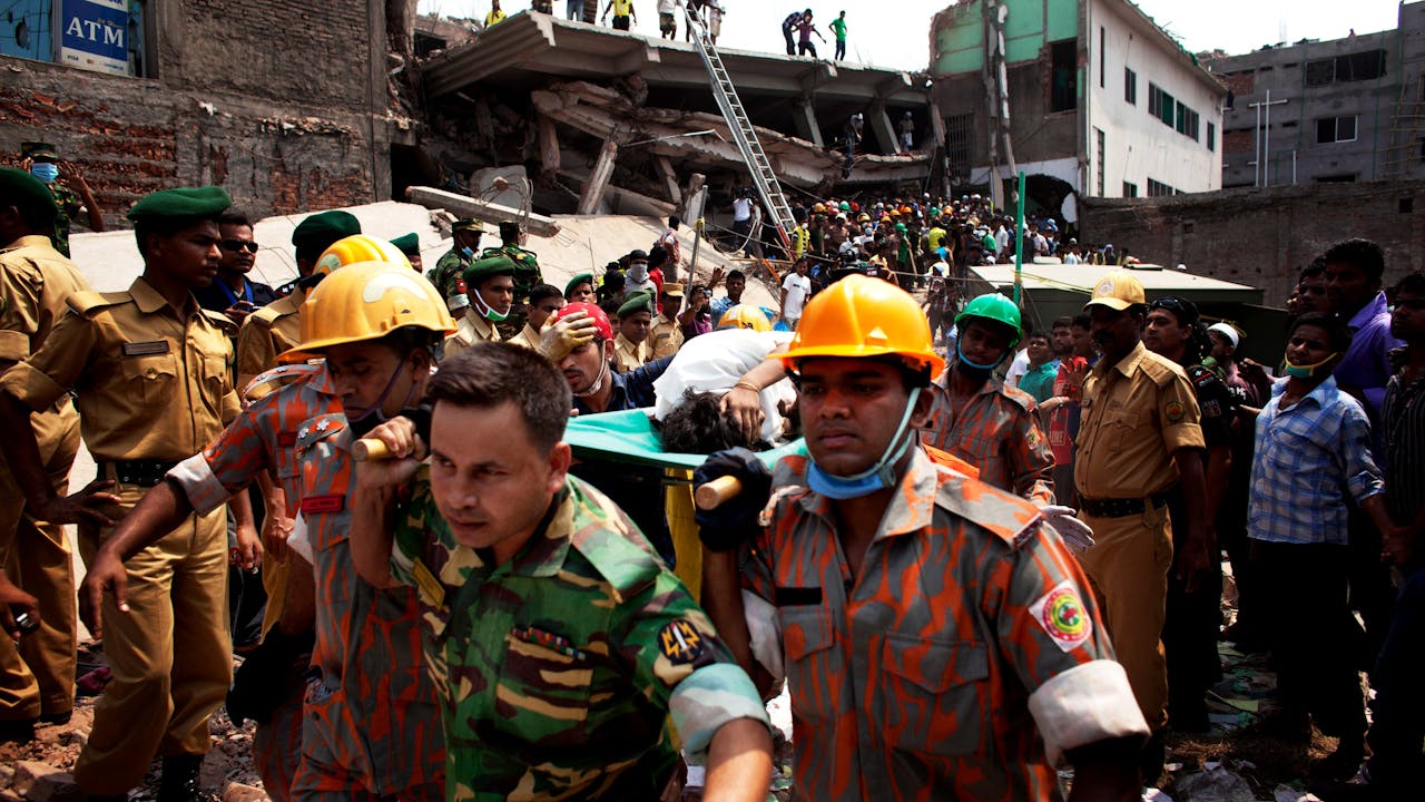 Members of Dhaka’s fire service carry an injured woman away from the rubble. In the background is the collapsed Rana Plaza building. 