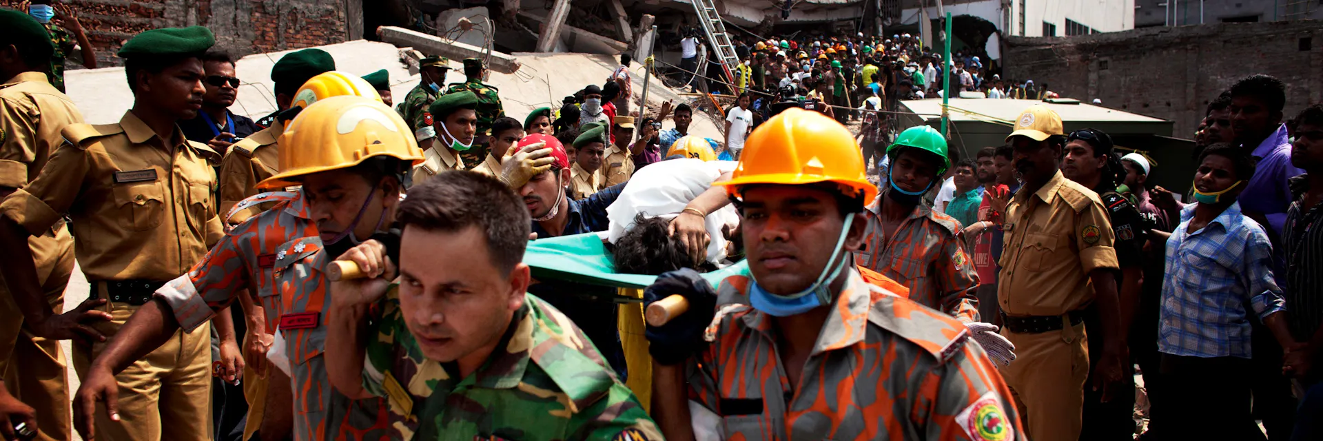 Members of Dhaka’s fire service carry an injured woman away from the rubble. In the background is the collapsed Rana Plaza building.