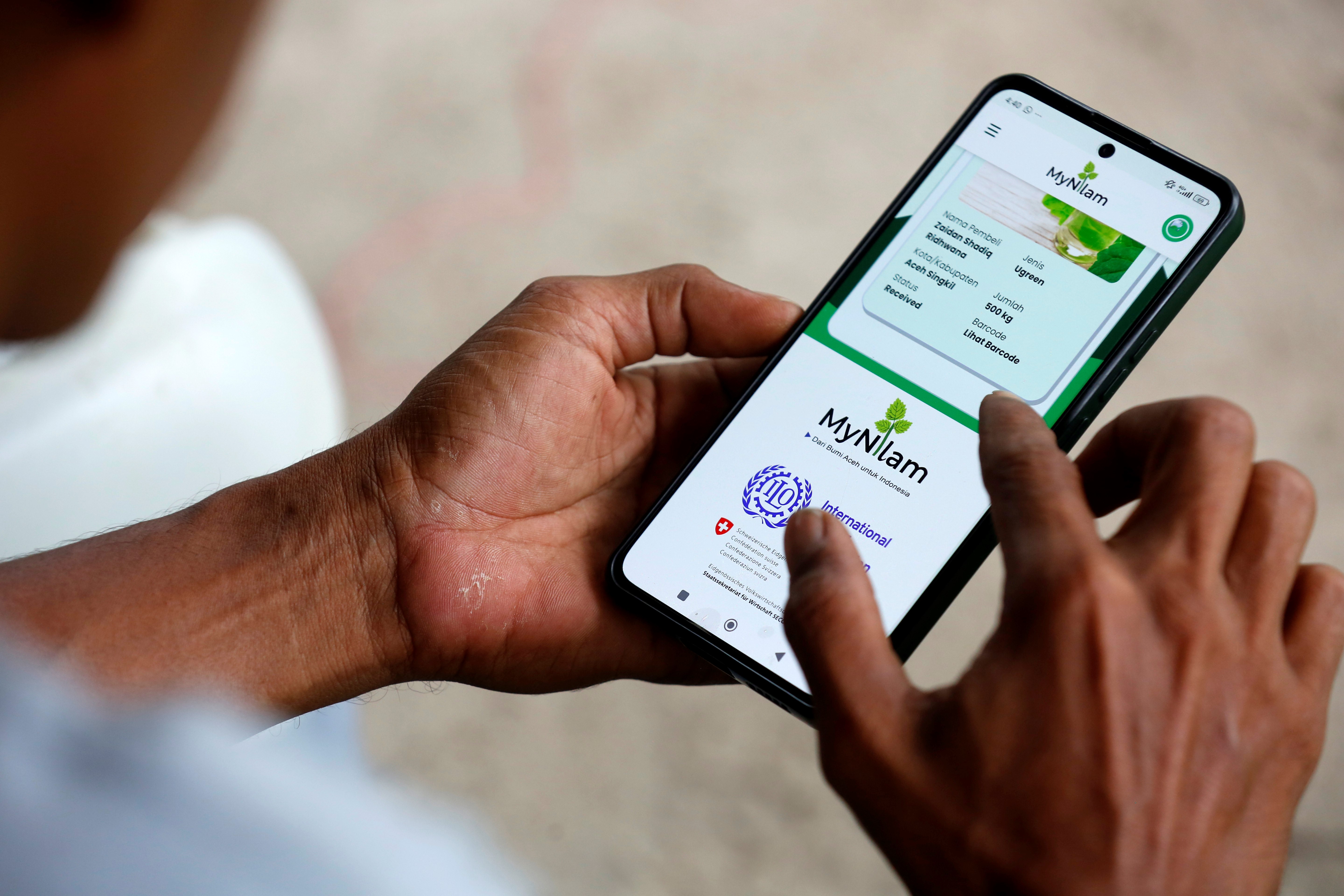 Teuku Razuan holds a telephone in his hands. He looks at the MyNilam app, launched by ILO.