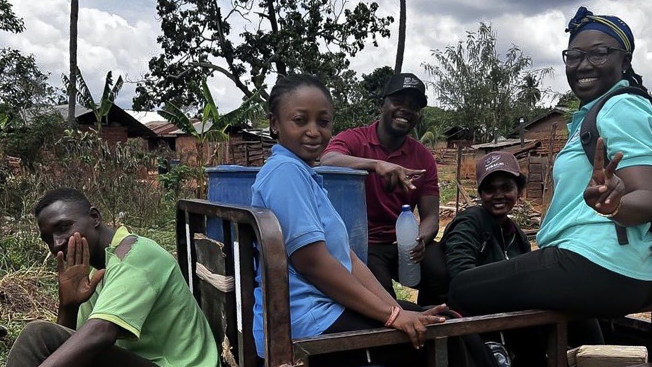 Kalian Sampoa Gumah wears a blue shirt and sits in the back of an open-top jeep with other enumerators.