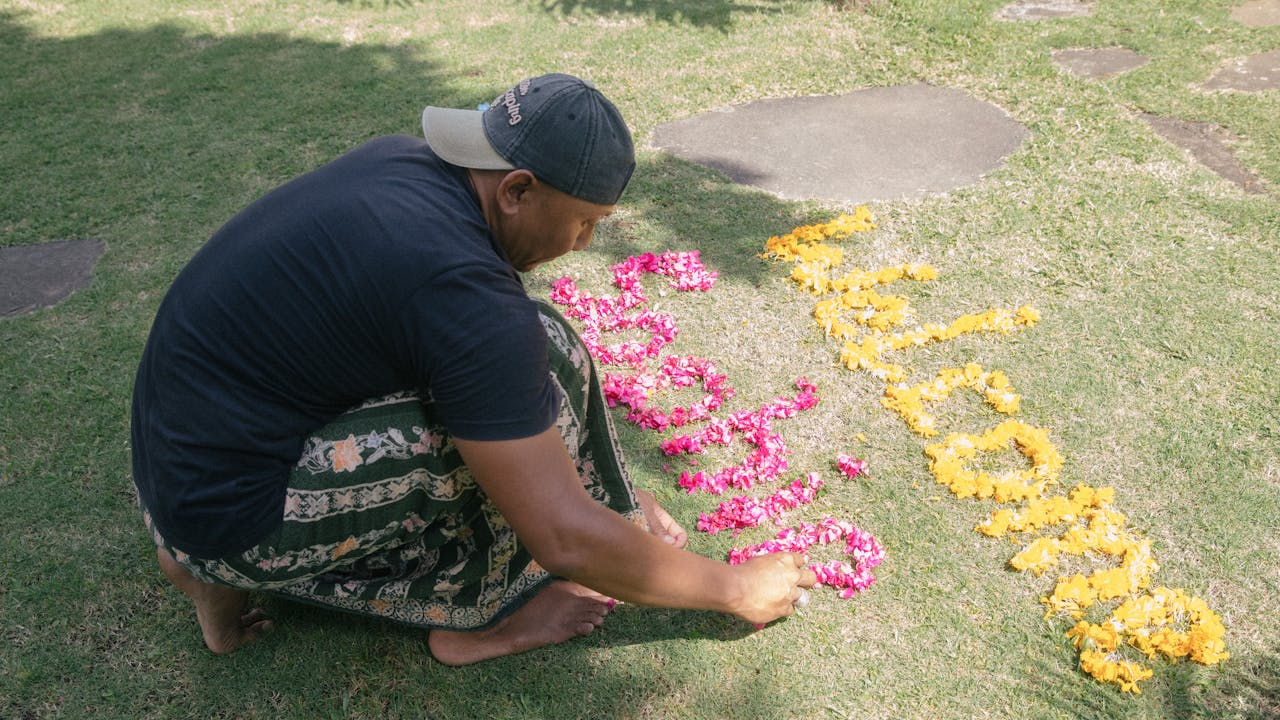 Dekha Dewandana squats on the ground and uses flower petals to write the words, "Welcome Sophie". 