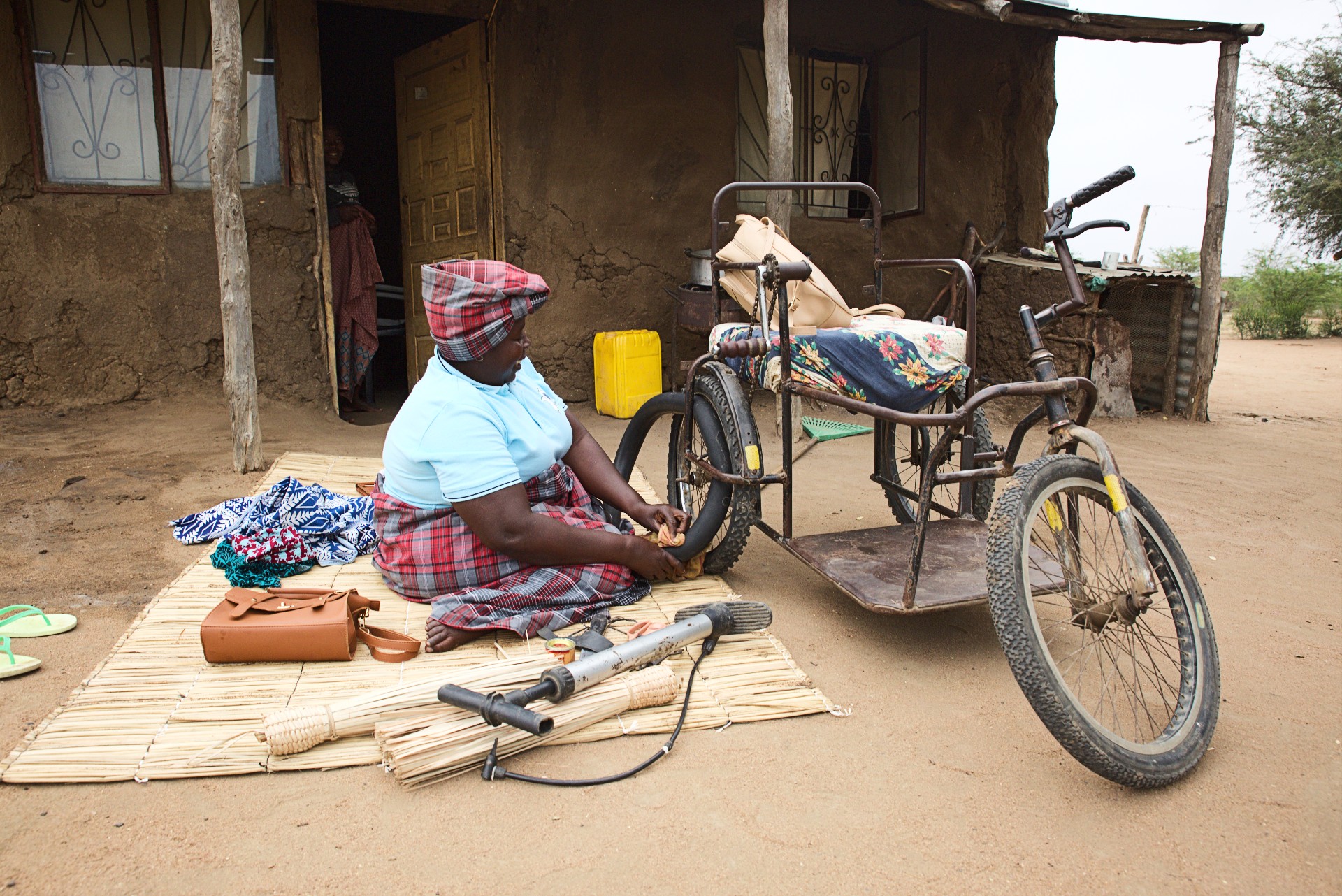 Linda Sarmento sits on the ground outside her house and repairs a puncture to the inner tube of one of the wheels of her wheelchair.