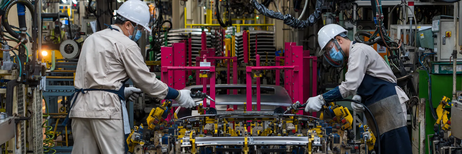 Two workers assemble car in car manufacturing plant.