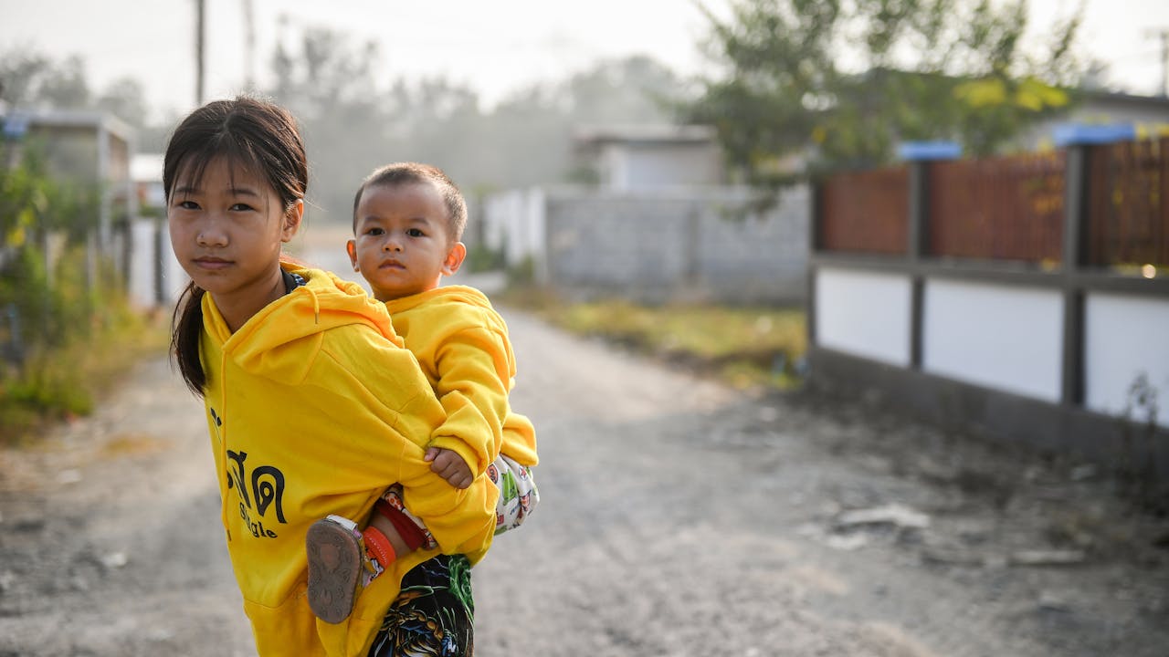 La fille de Sai Sai, âgée de 12 ans, se tient sur la route et porte son petit frère sur son dos. Tous deux regardent droit dans la caméra.