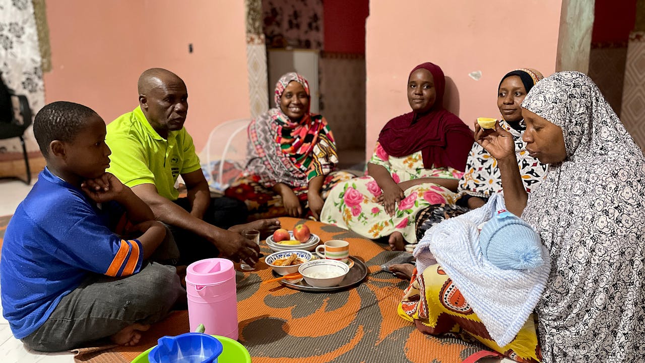 Hussein Juma Hassan y su familia sentados en círculo comparten una comida. 