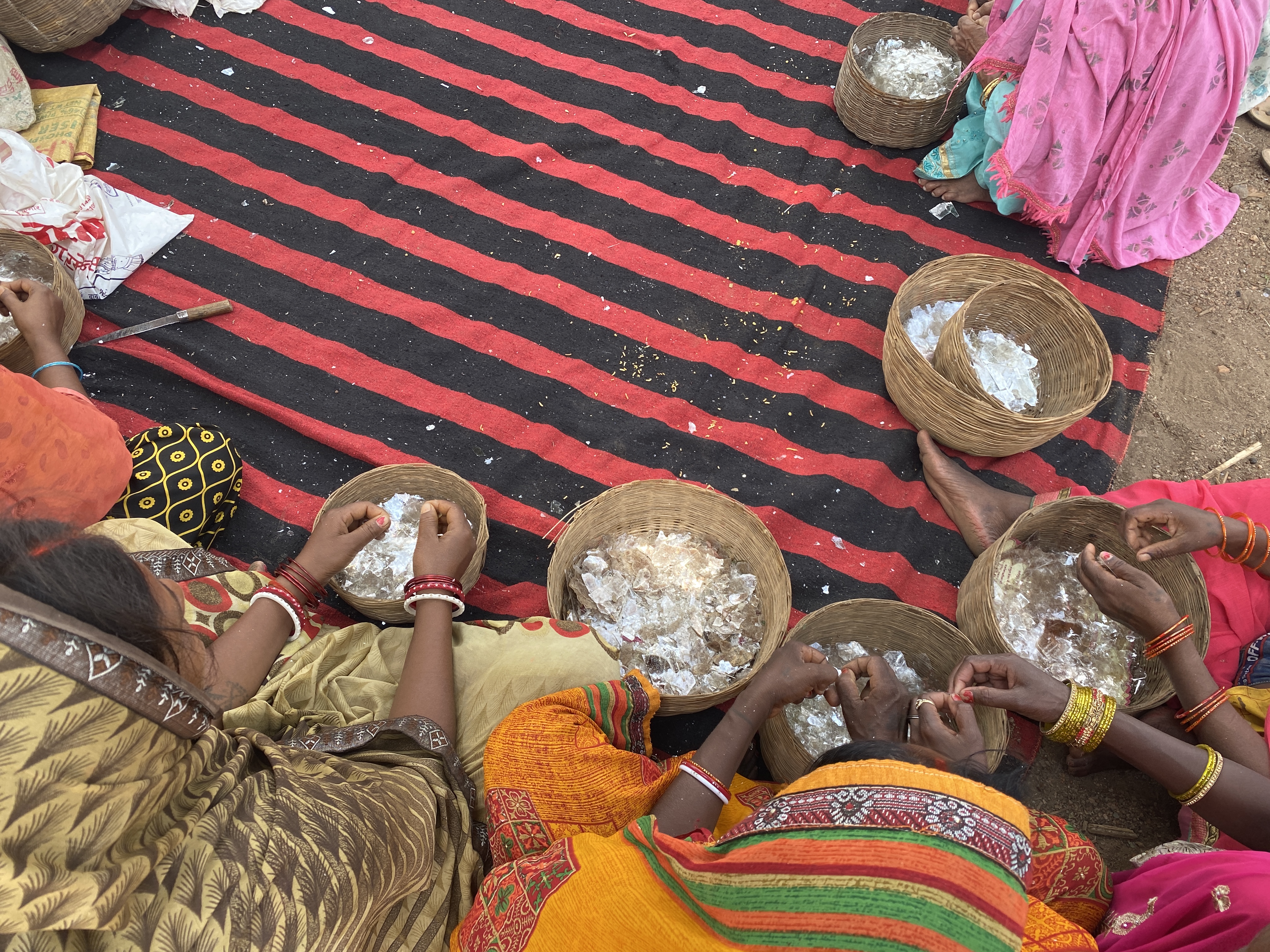 A circle of women sit cross-legged and sort through baskets of mica flakes.