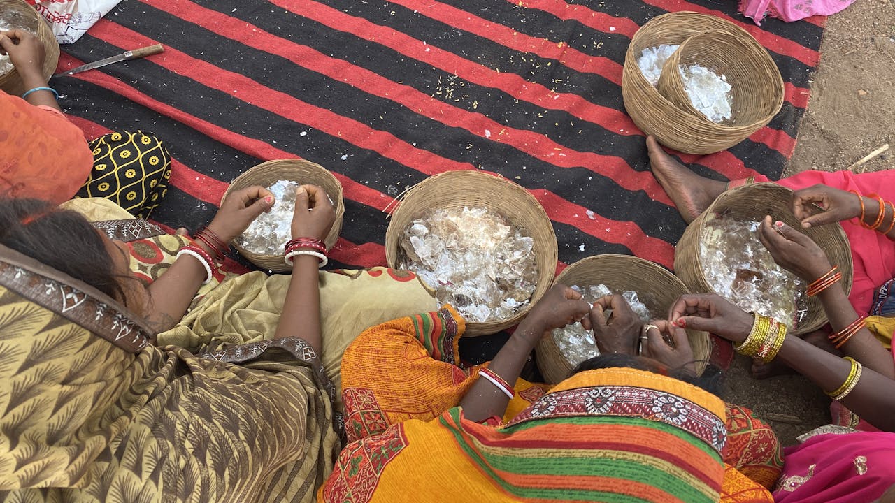 A circle of women sit cross-legged and sort through baskets of mica flakes.