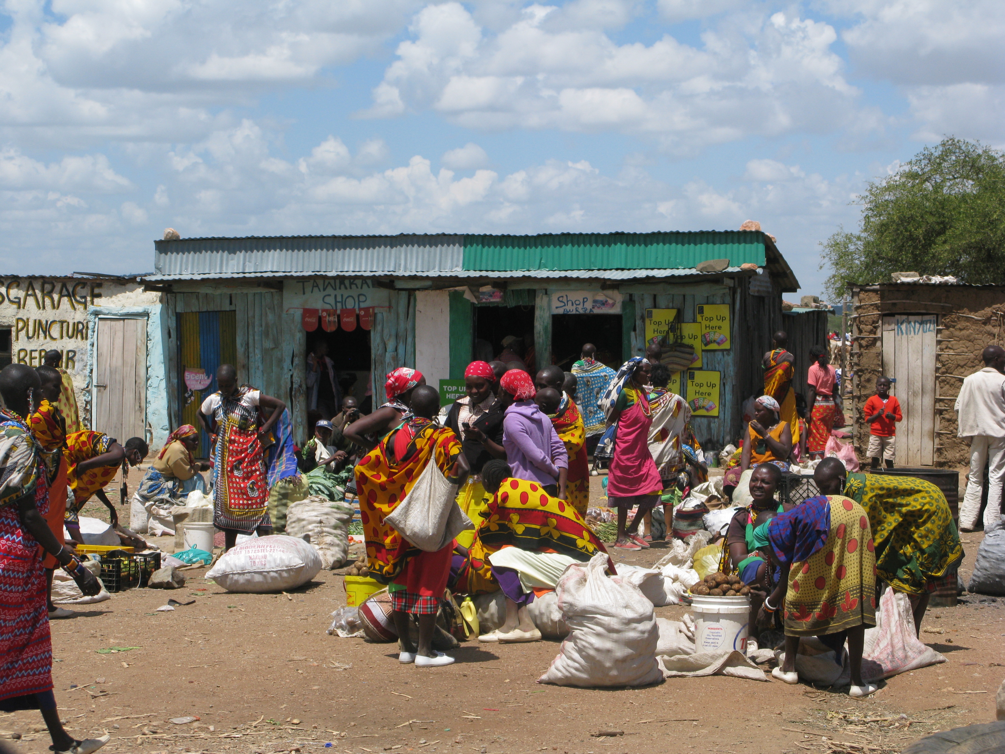 Market day in a Maasai village. Many Maasai women are gathered buying and selling food, including potatoes.