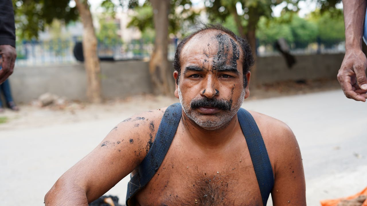 A portrait of Shafique Massih. He has just been working in a sewer. There is raw sewage spattered on his face. He is shirtless, but wears a harness over his shoulders, which is used to pull him out of the sewer in an emergency.