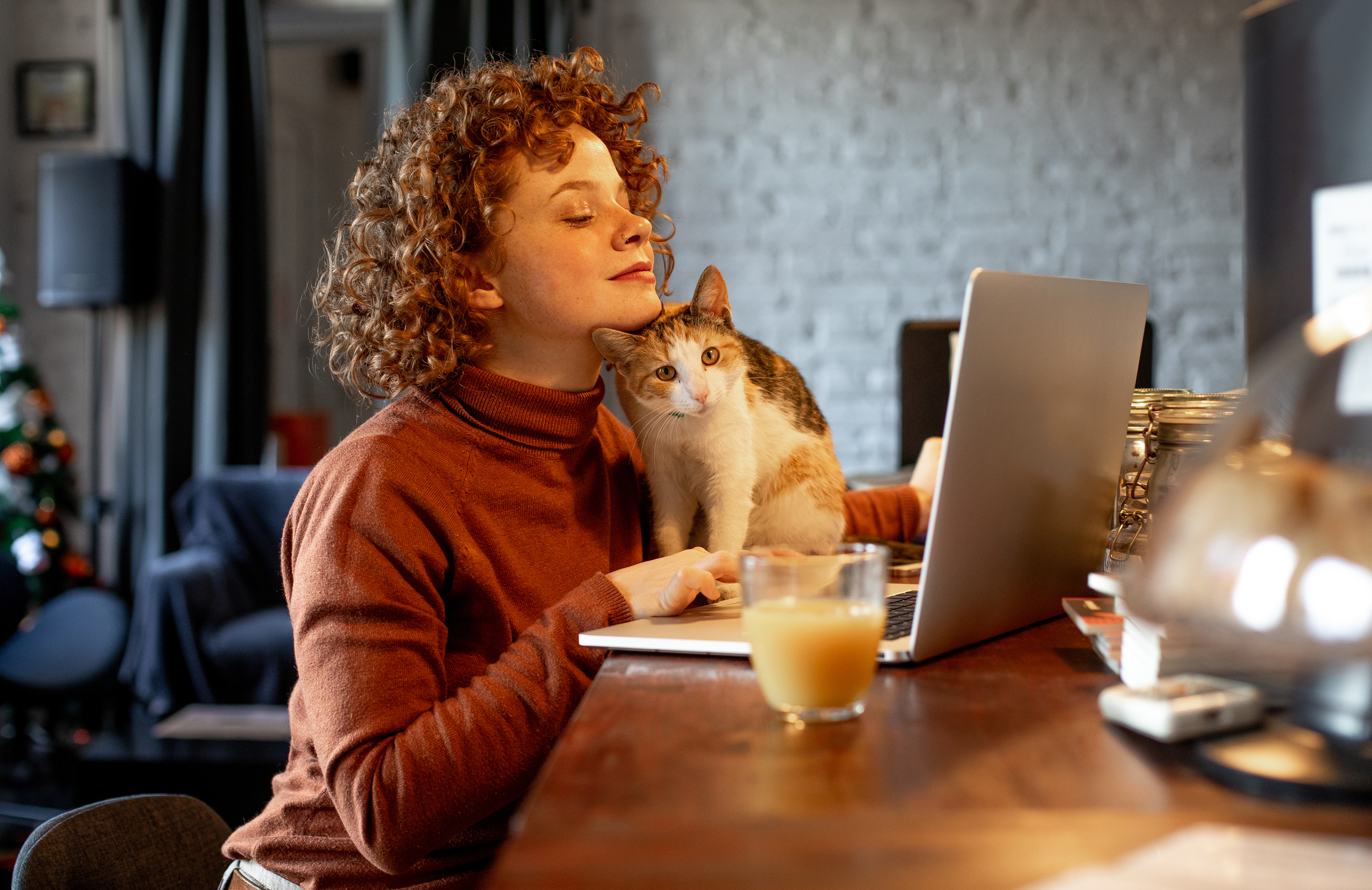 A young woman is working using a laptop and her cat is sat next to her.