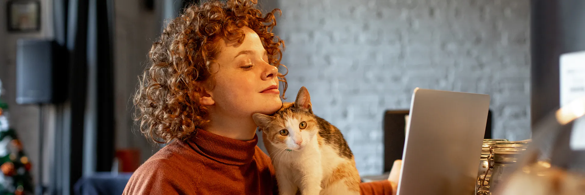 A young woman is working using a laptop and her cat is sat next to her.