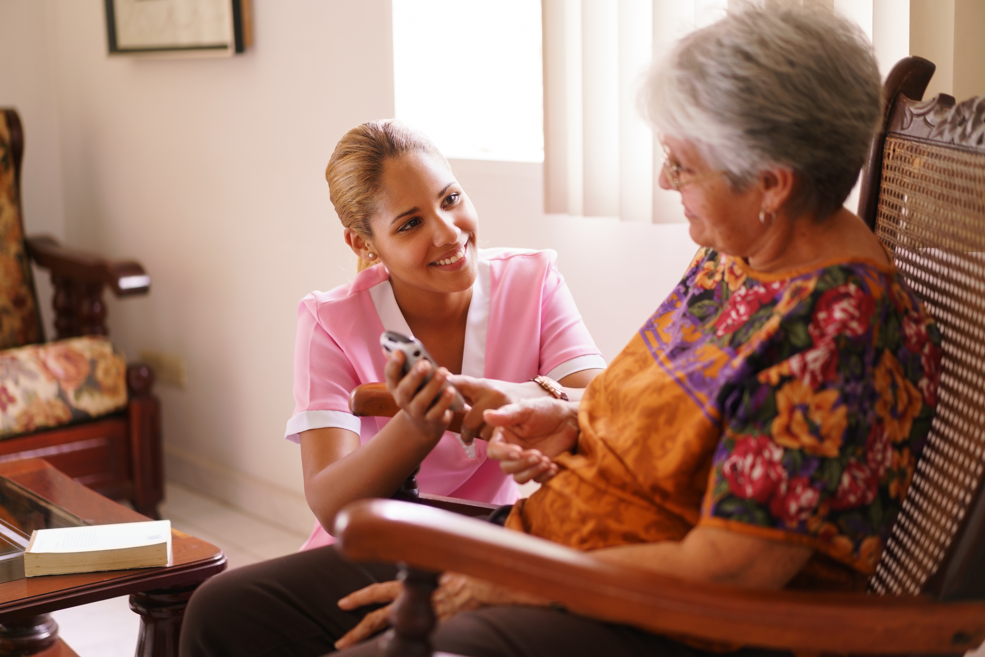 A care worker helps an elderly woman use a mobile device.  