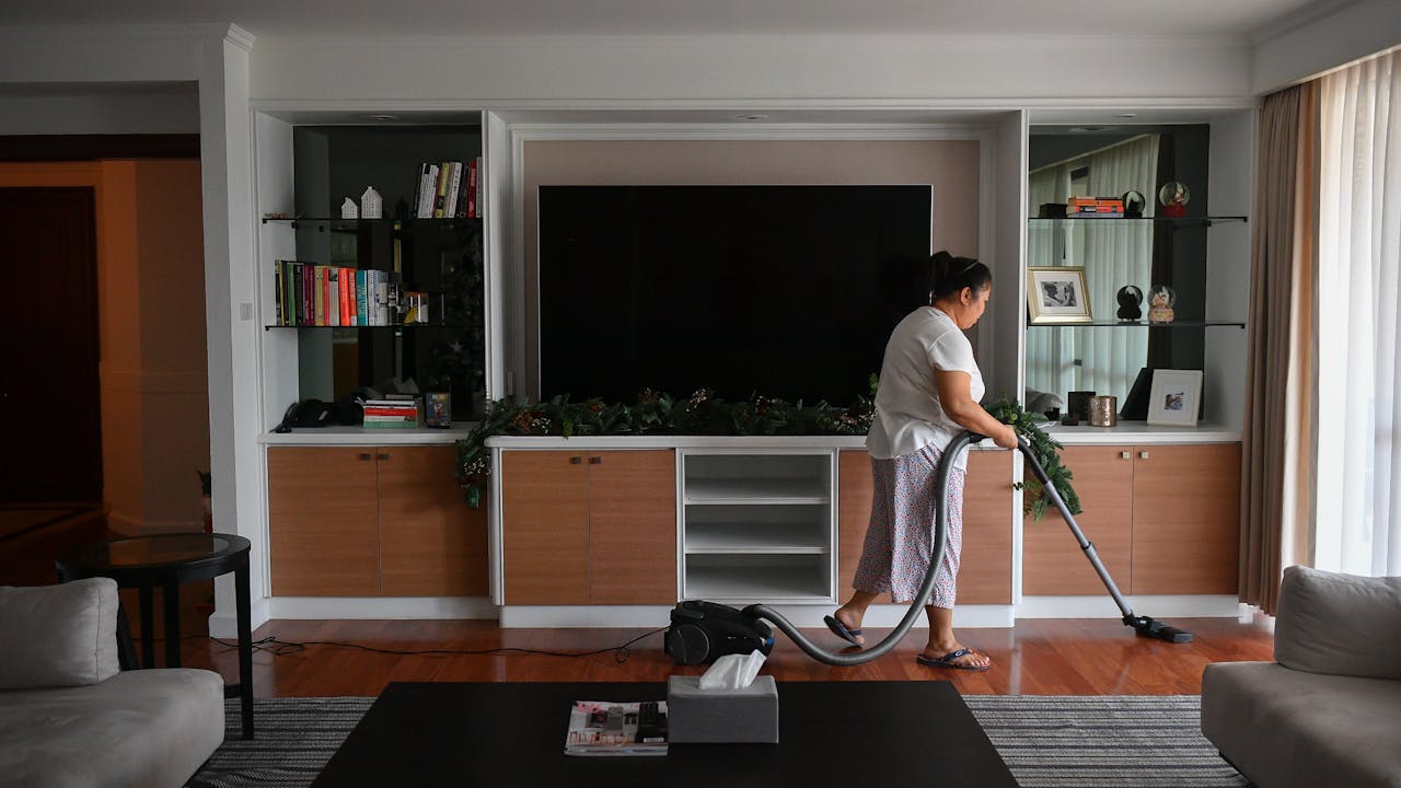 Champa hoovers in her employer’s living room, with a widescreen television in the background.