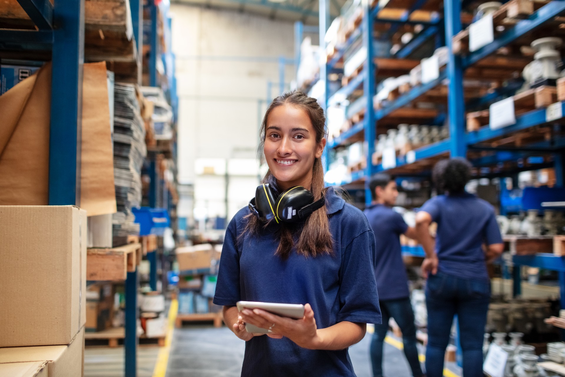 Portrait d'un ouvrier d'usine avec une tablette numérique regardant la caméra et souriant. Employé d'entrepôt avec des gens en arrière-plan.