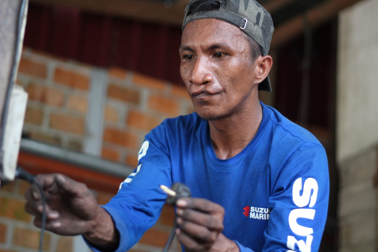 Un homme à la lèvre déformée branche un câble électrique dans l’atelier de réparation.
