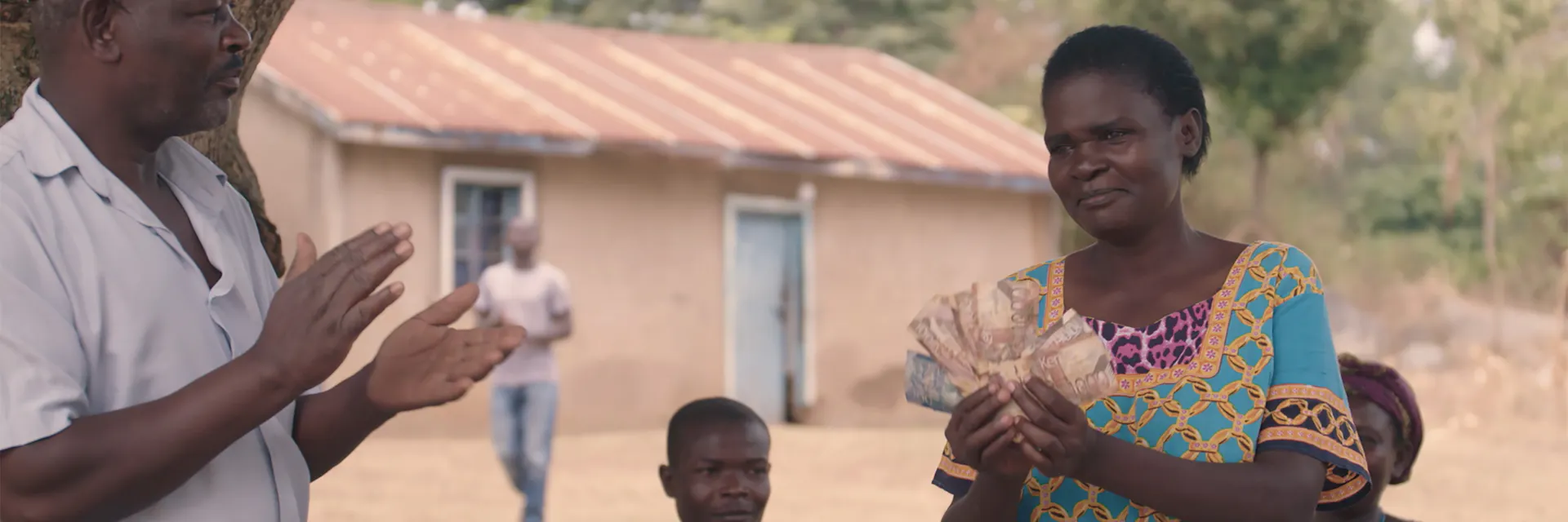 A Kenyan woman in the village of Kogutu stands while holding up banknotes as other villagers applaud.