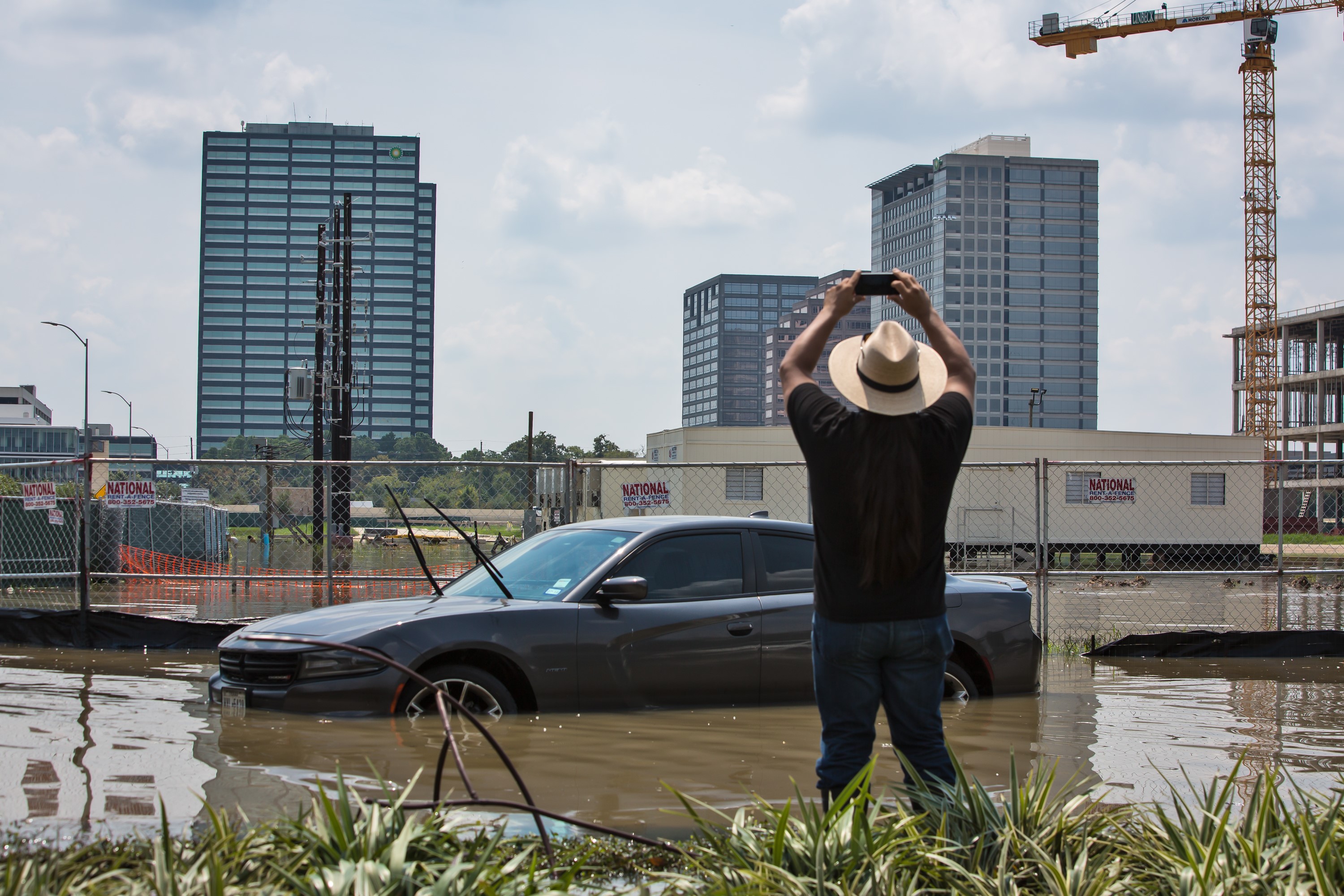 Bryan Parras takes a photo of a car in a flooded parking lot with skyscrapers of Houston in the background.