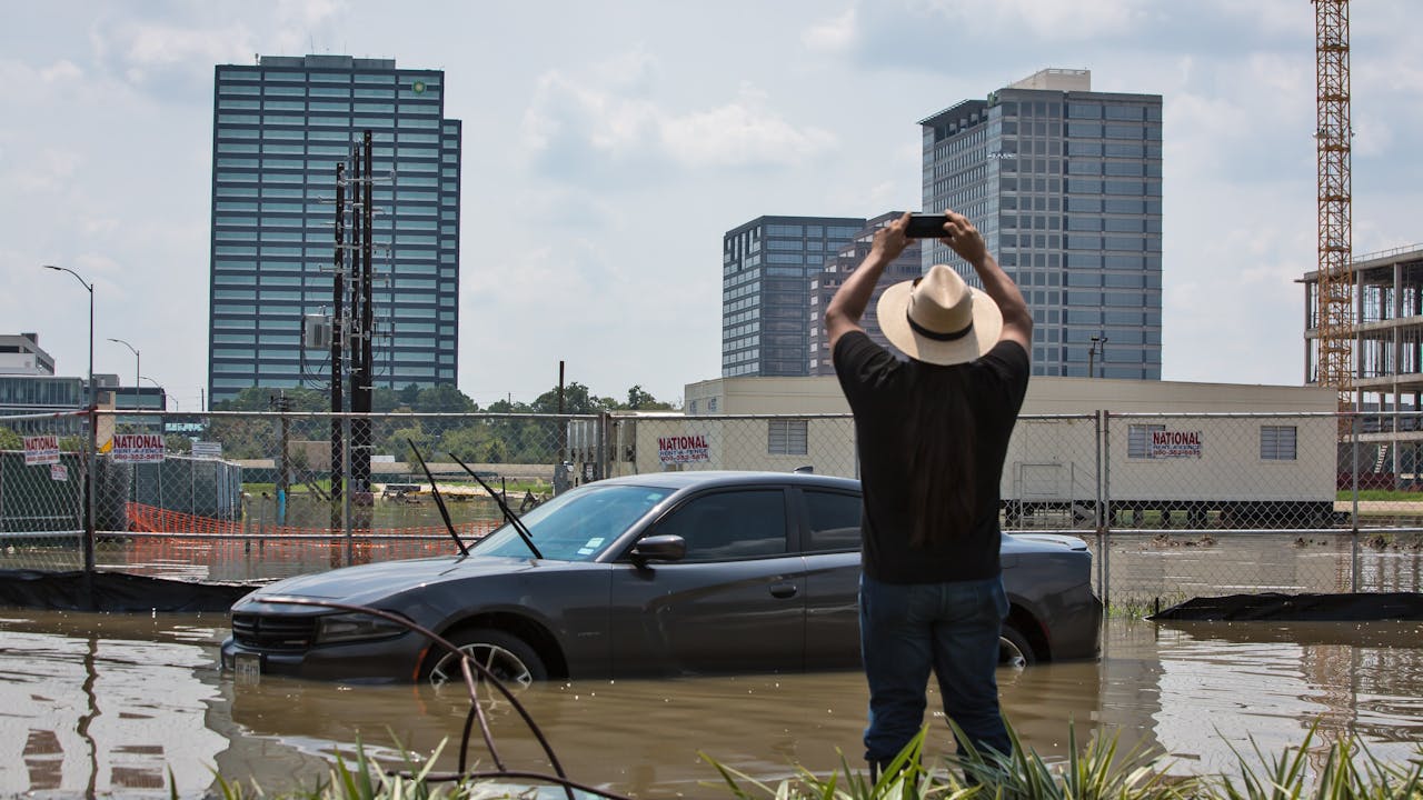 Bryan Parras takes a photo of a car in a flooded parking lot with skyscrapers of Houston in the background.