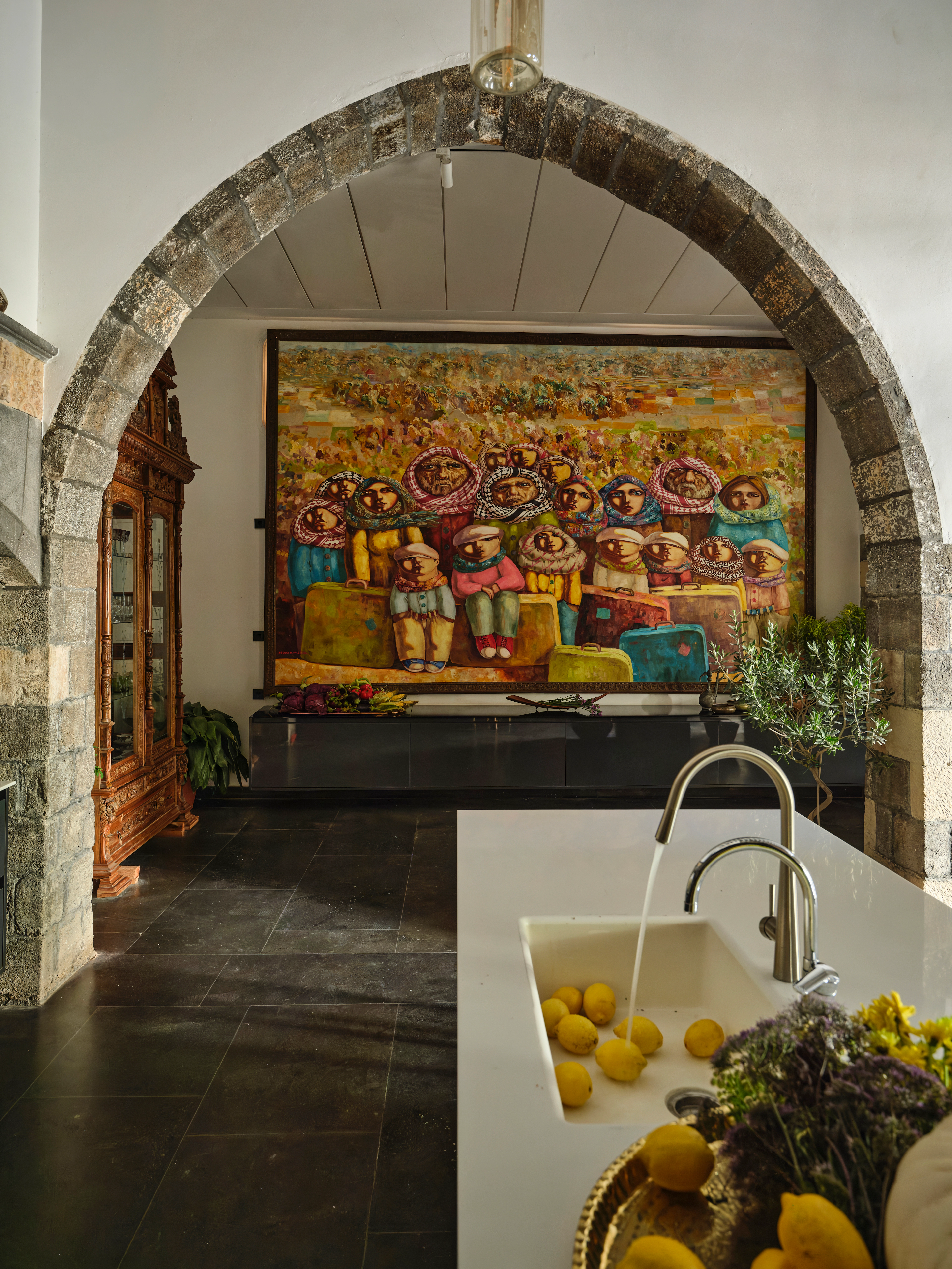 Kitchen with a stone archway, white island, colorful artwork, and lemons arranged beside the sink.