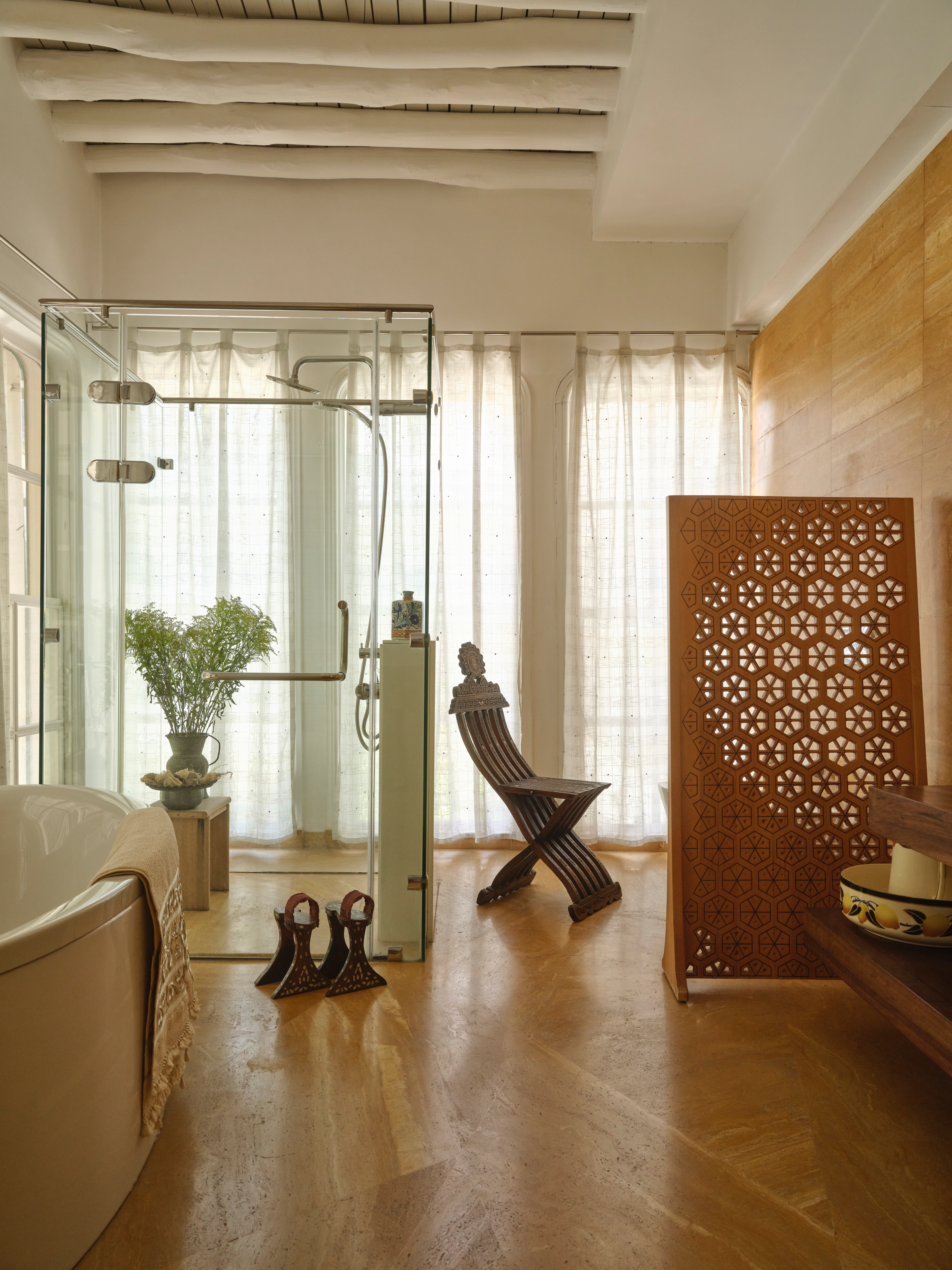 Bright bathroom with a freestanding tub, glass shower, carved wooden screen, and sculptural wooden chair.