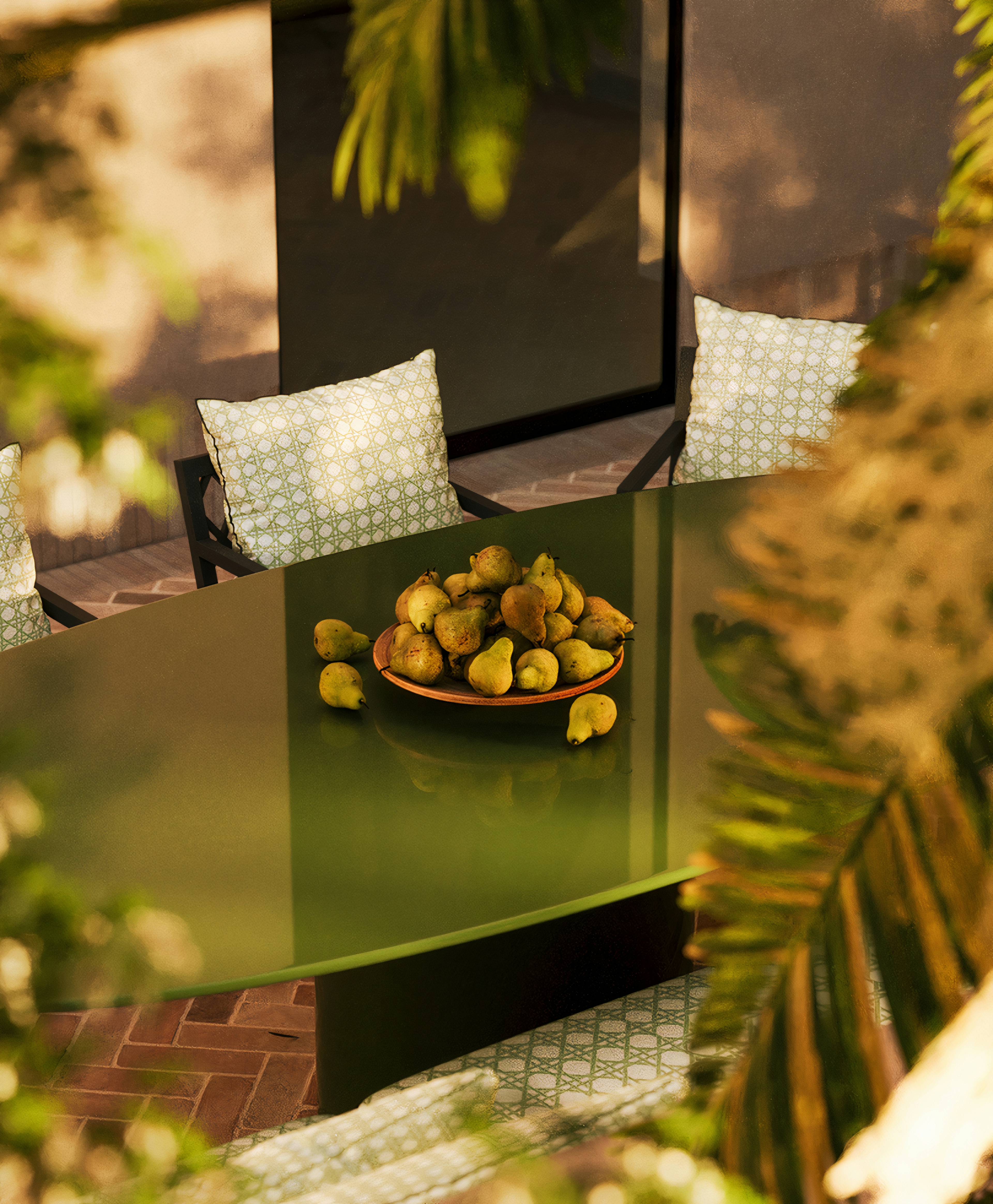 Dining table with glossy green top, surrounded by patterned cushions, styled with a bowl of pears.