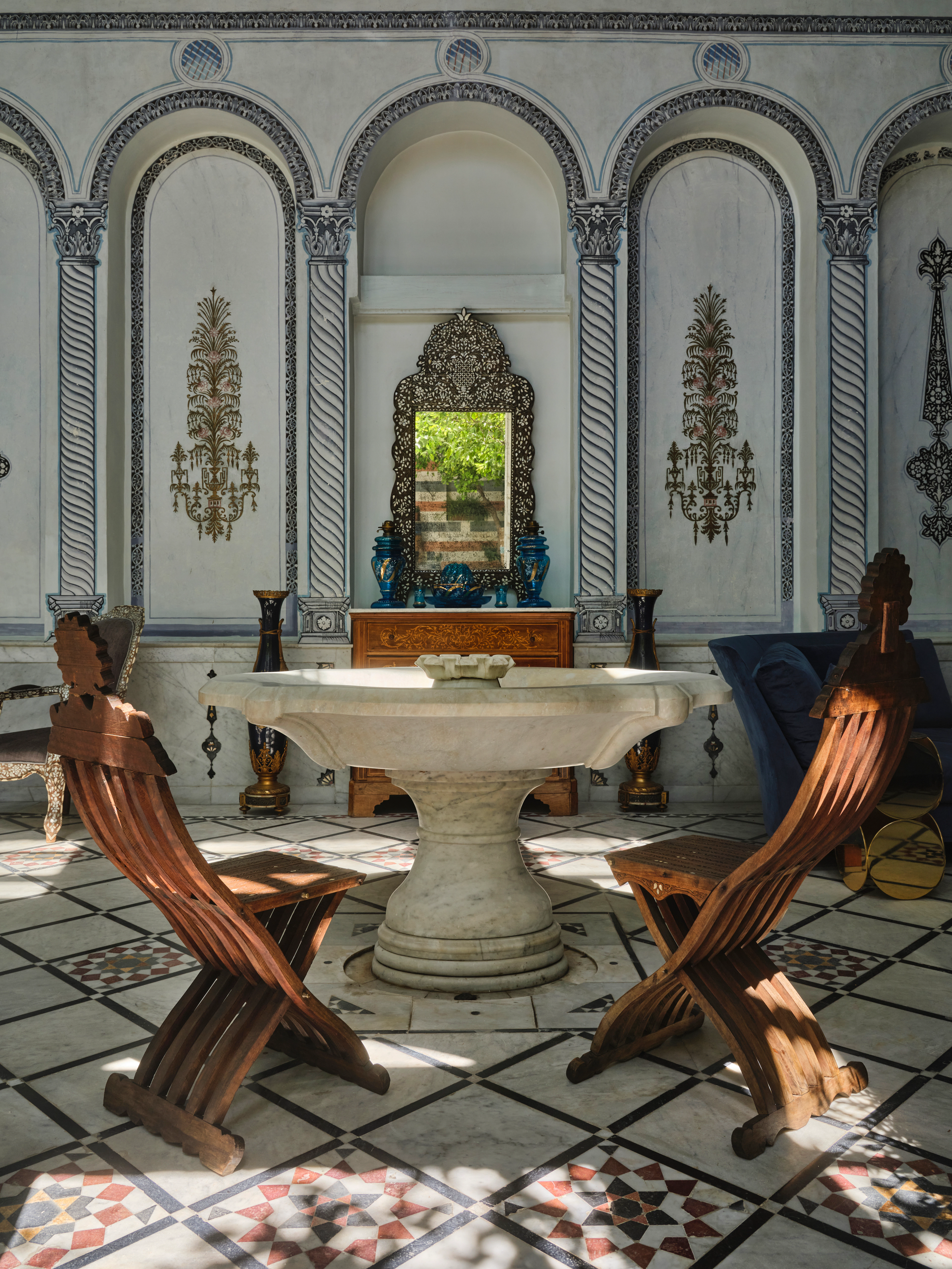 Blue and white salon with arched alcoves, a central stone table, patterned tile floor, and carved wooden chairs.