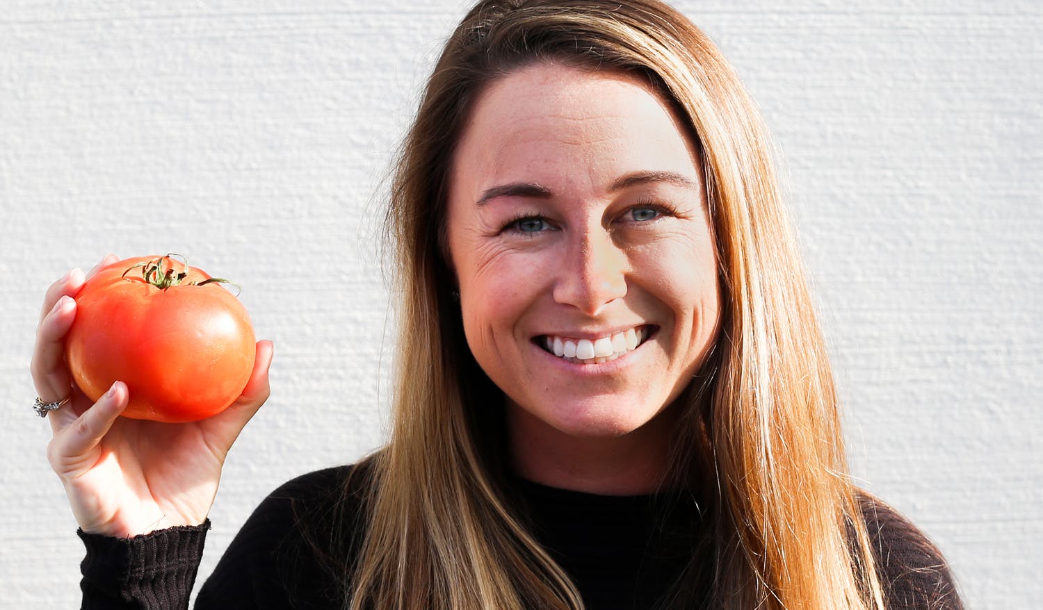 Jamie smiling and holding up a tomato.