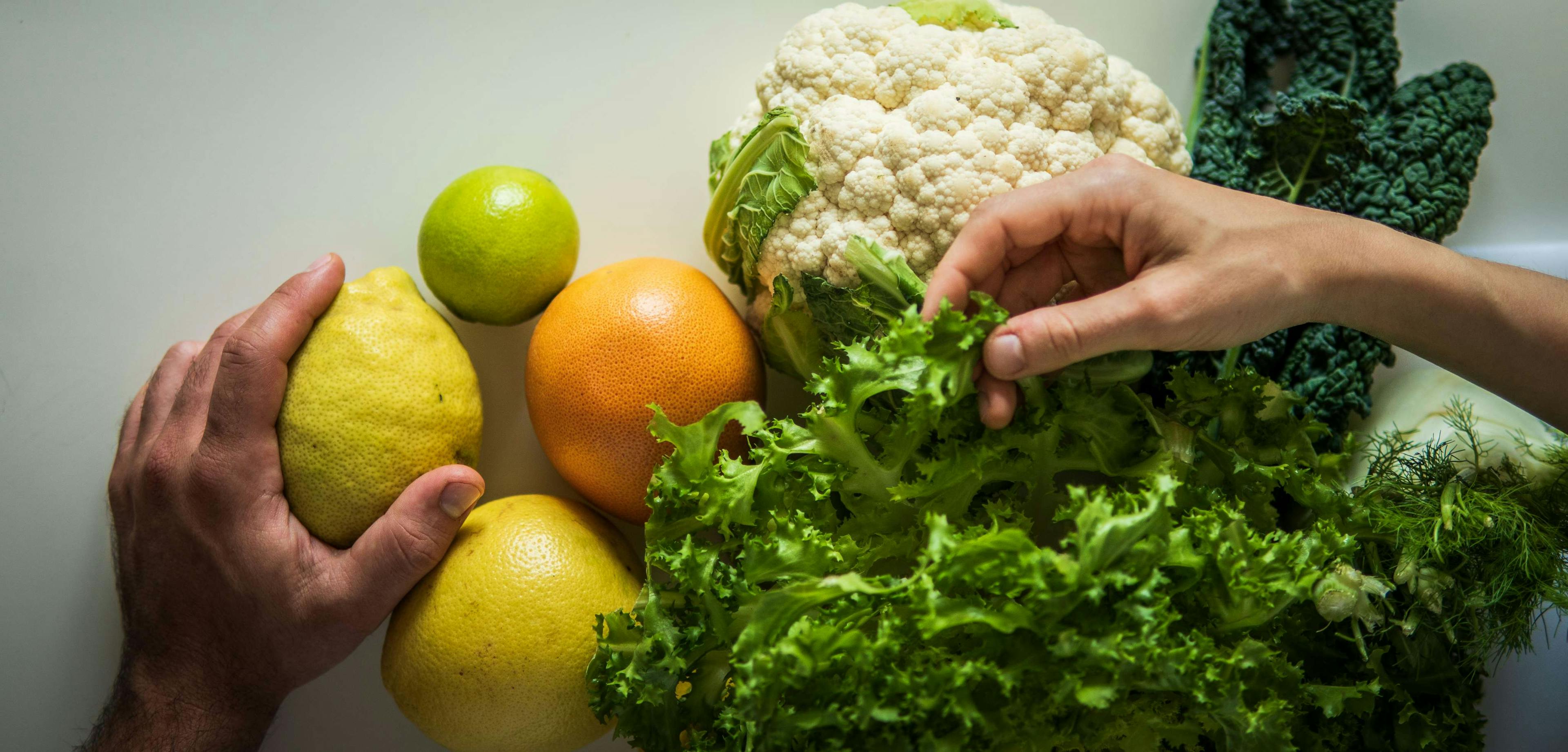 Le mani degli chef di Impronta che toccano alcuni ingredienti colorati con sfondo bianco.
