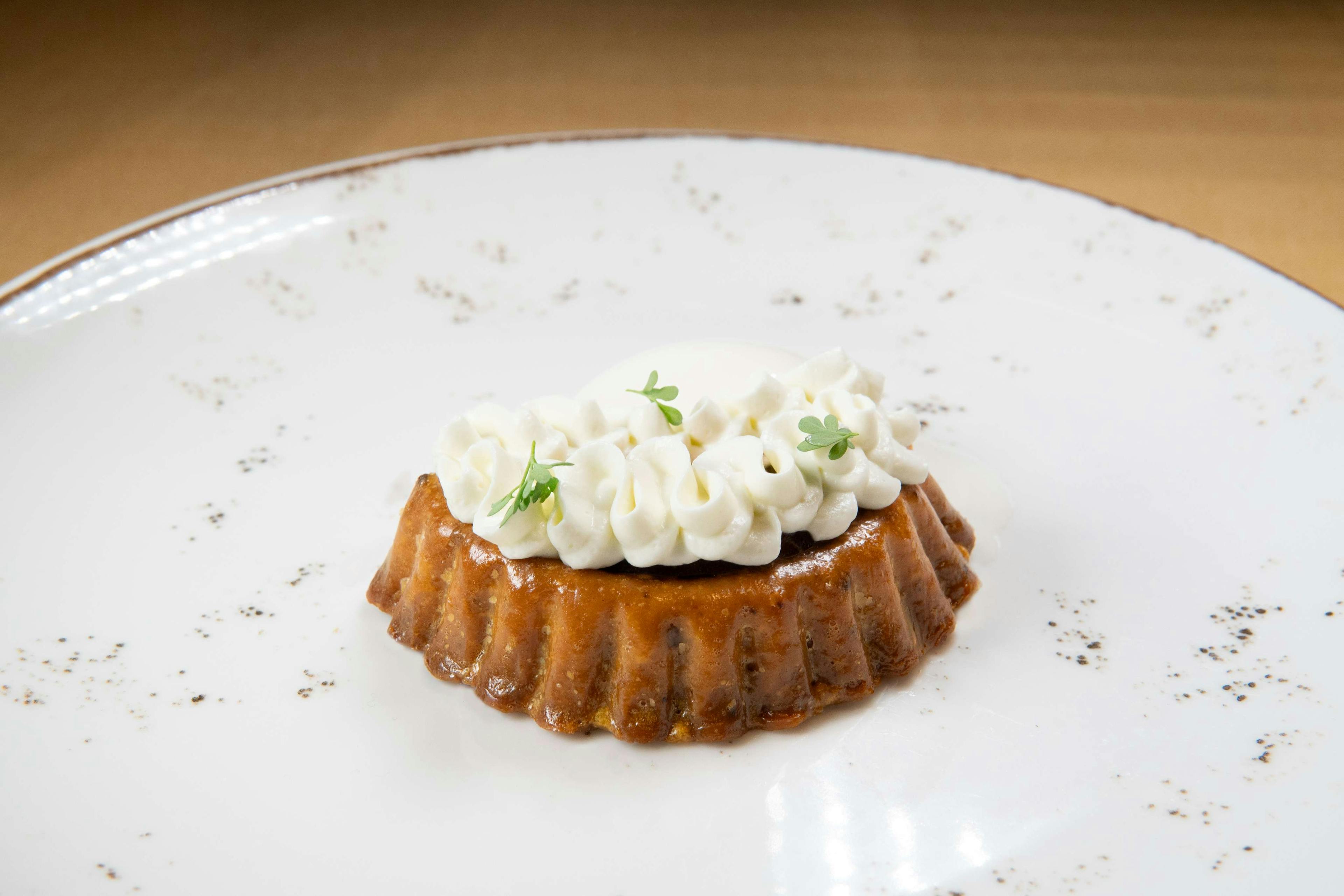 La foto rappresenta un dolce di Impronta, composto da una tartelletta e una mousse, su un piatto bianco con puntini scuri.