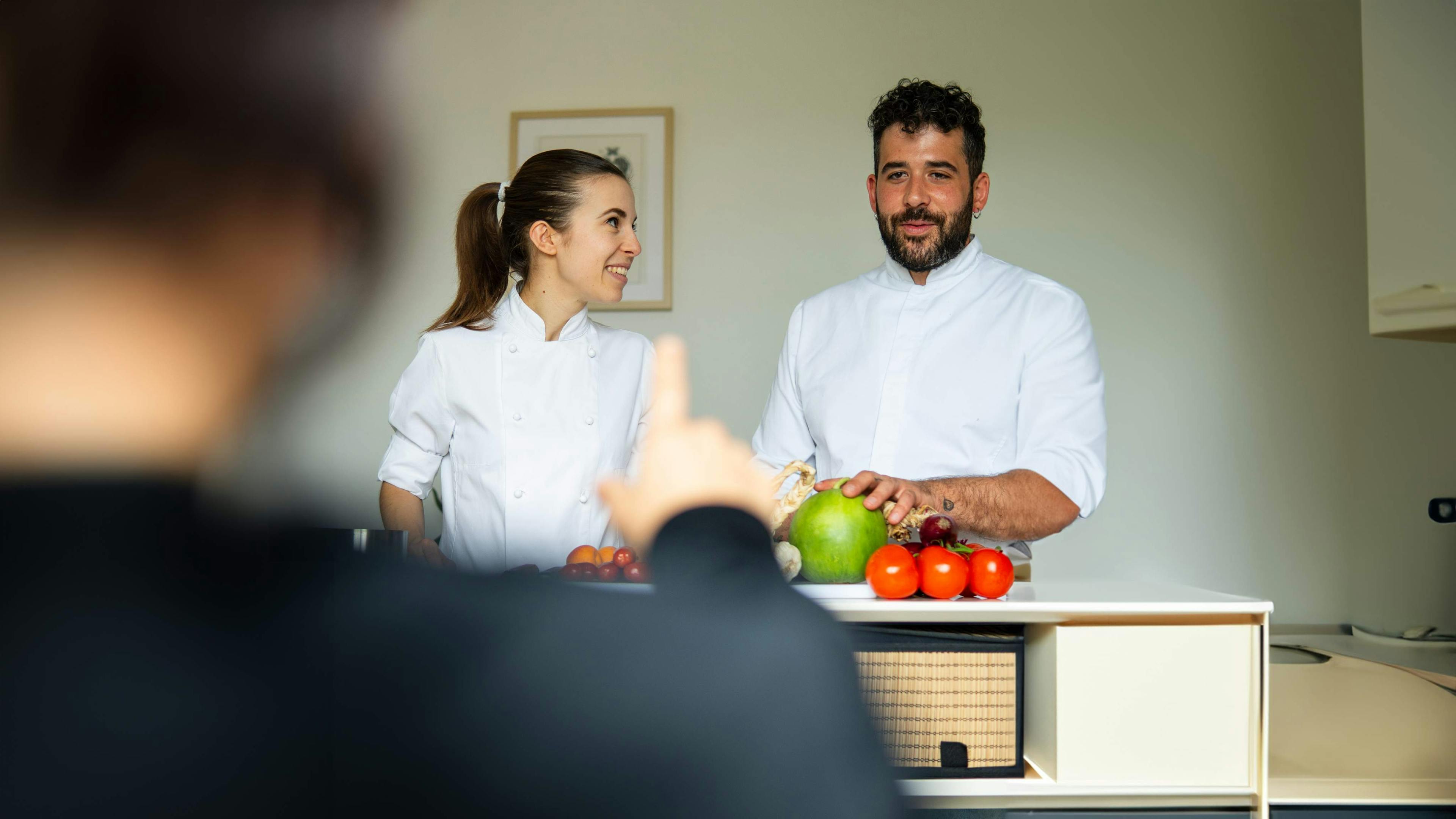 Valeria Loi e Gabriel Cinque, chef e founder di Impronta, in divisa da lavoro (giacca bianca) mentre tengono una lezione.