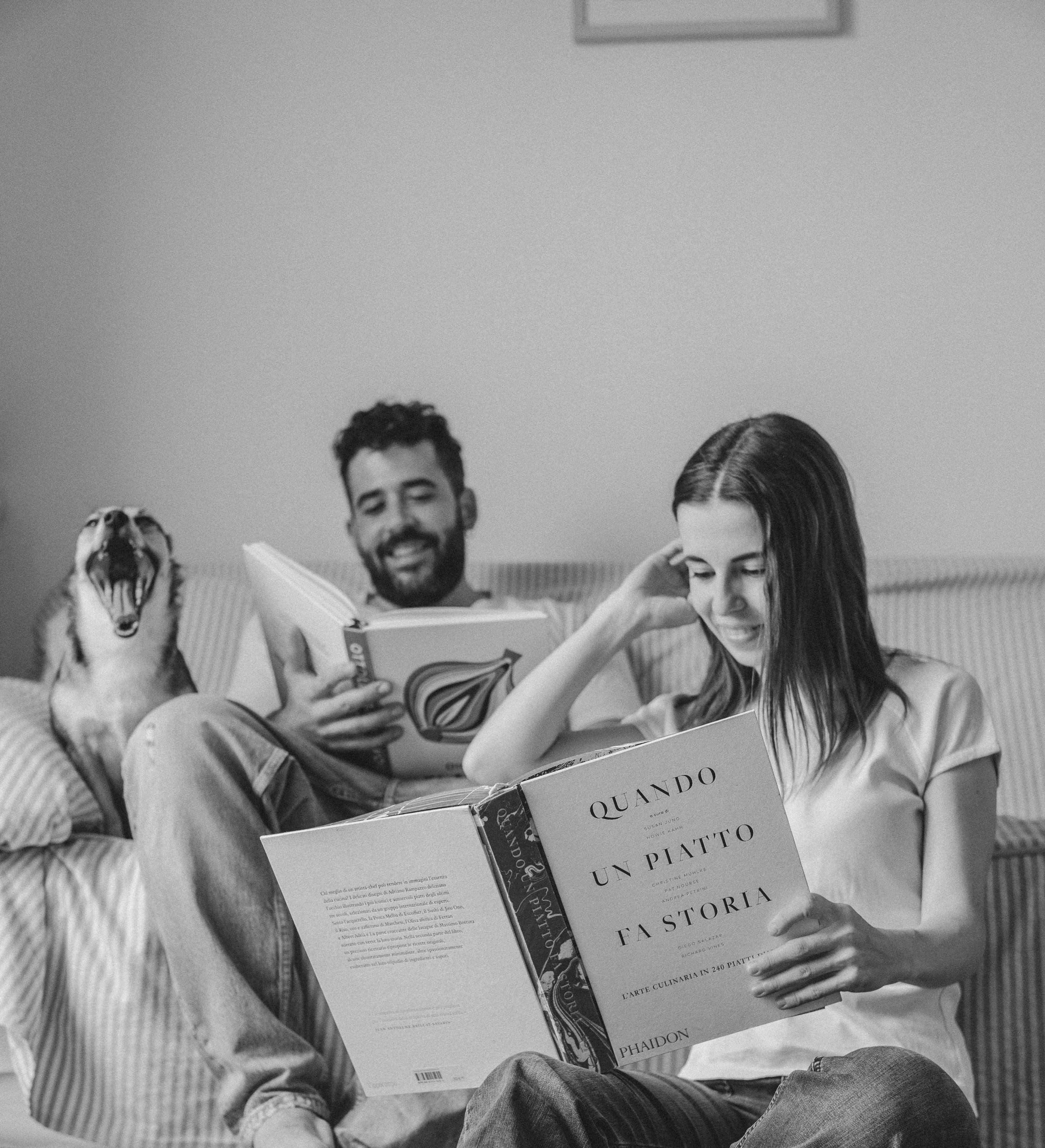 Gabriel Cinque e Valeria Loi, chef e founder di Impronta, su un divano mentre leggono libri di cucina insieme al loro cane.