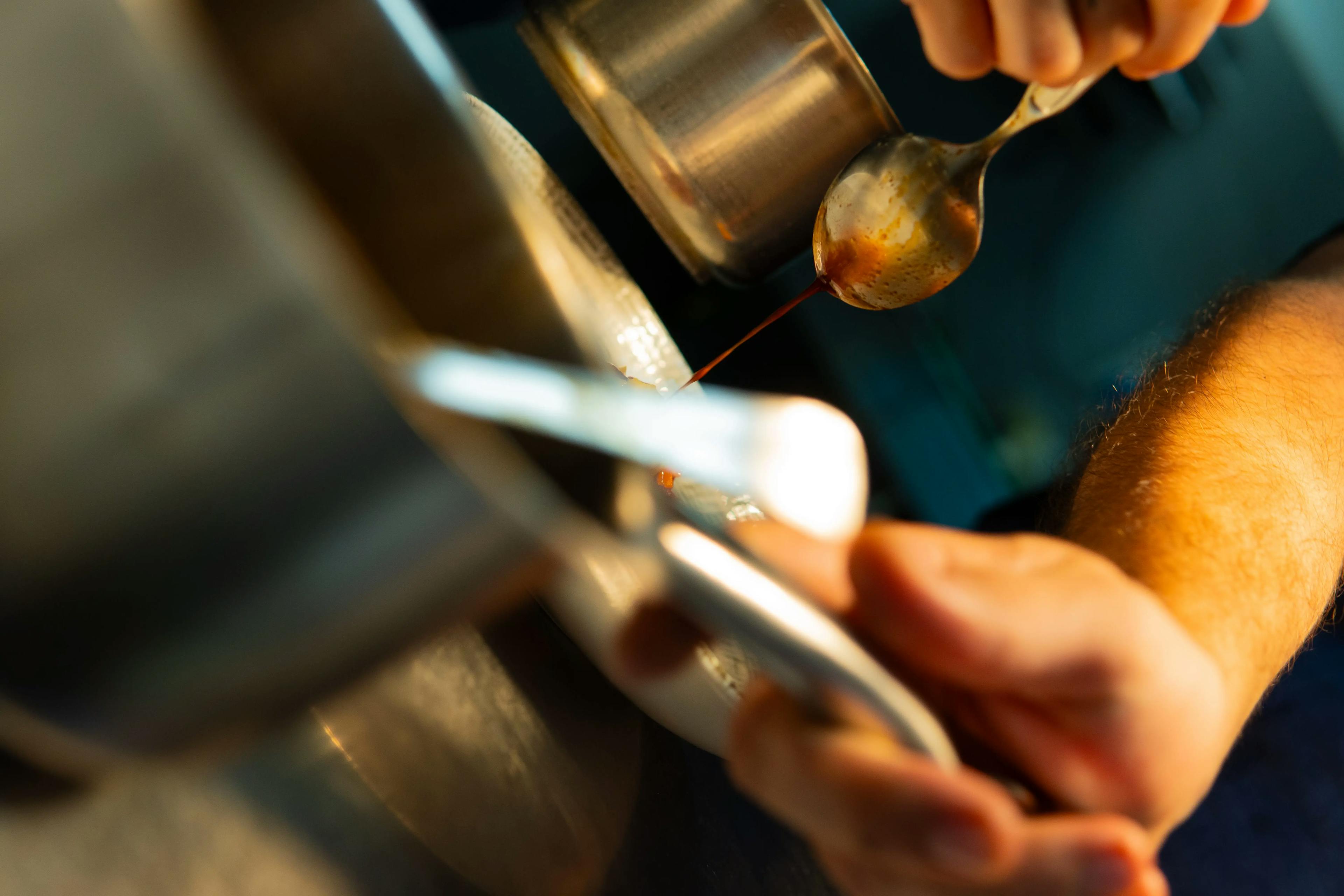 Foto molto ravvicinata di un cucchiaio che versa una salsa e un braccio di un persona che sta lavorando durante un servizio.