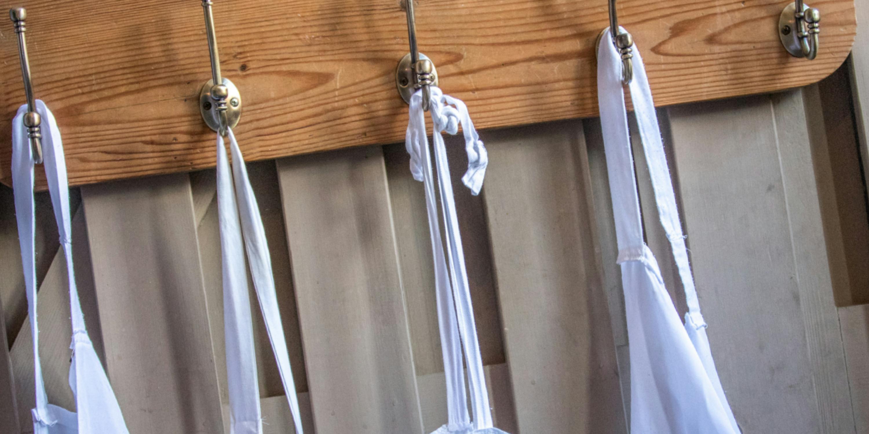 Foto di quattro grembiuli bianchi da cucina appesi a un appendiabiti da muro in legno.