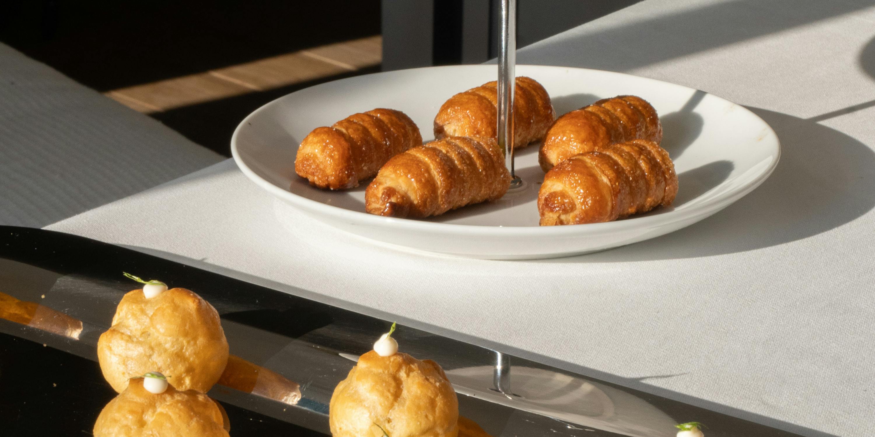 Buffet di finger food allestito su un tavolo con tovaglia bianca. Ci sono bignè salati e cannoncini di sfoglia.