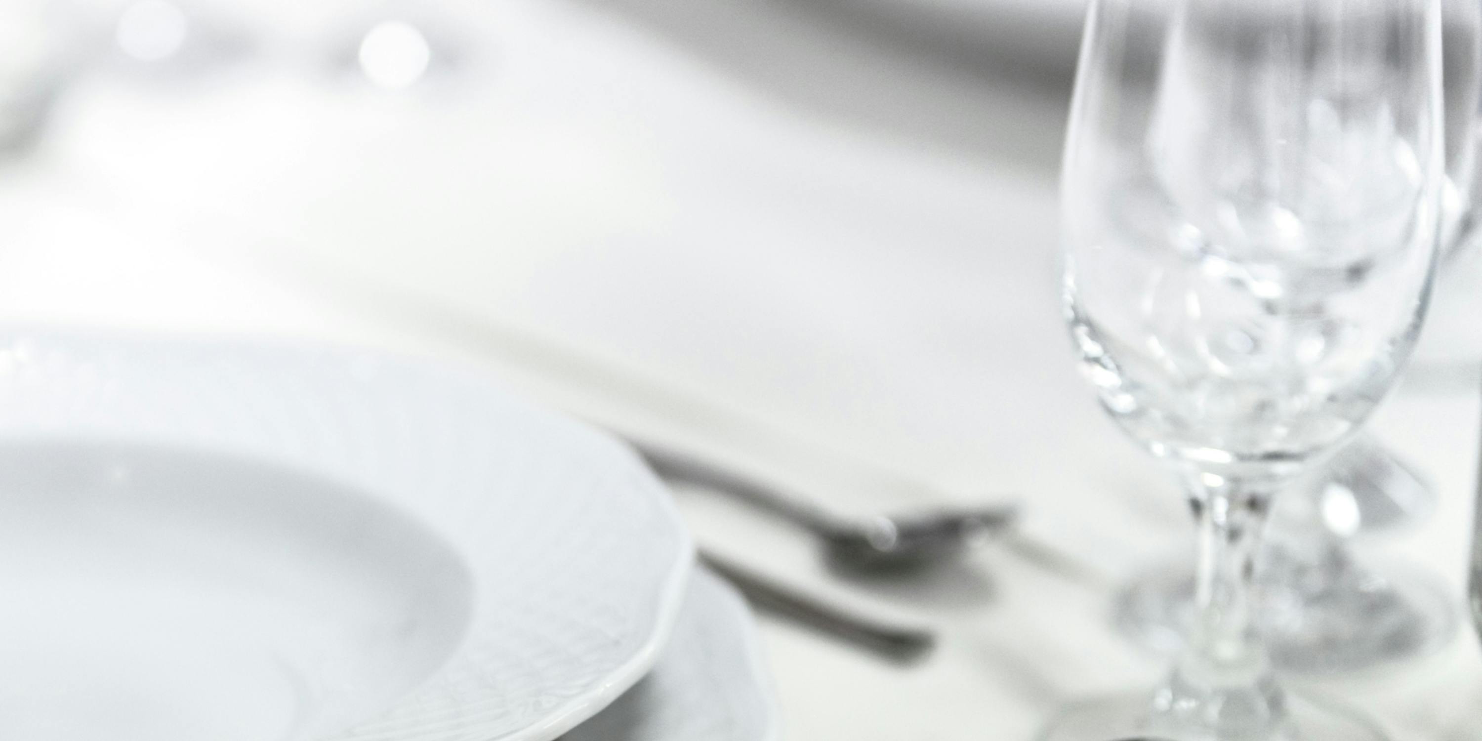 Dettaglio di un tavolo apparecchiato con grande eleganza: tovaglia bianca, piatti bianchi, bicchieri di cristallo.