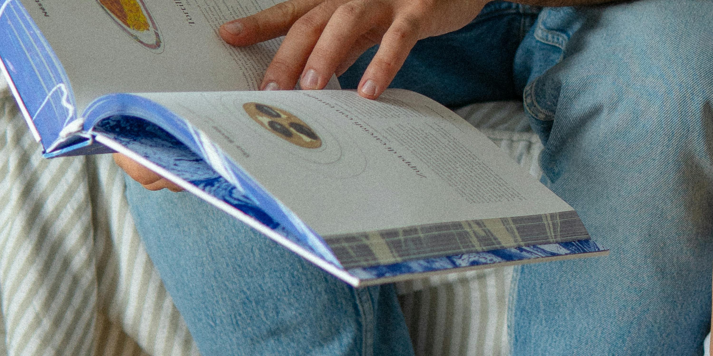 Il libro "Quando un piatto fa la storia" è aperto e sfogliato da una persona che indossa jeans chiari.